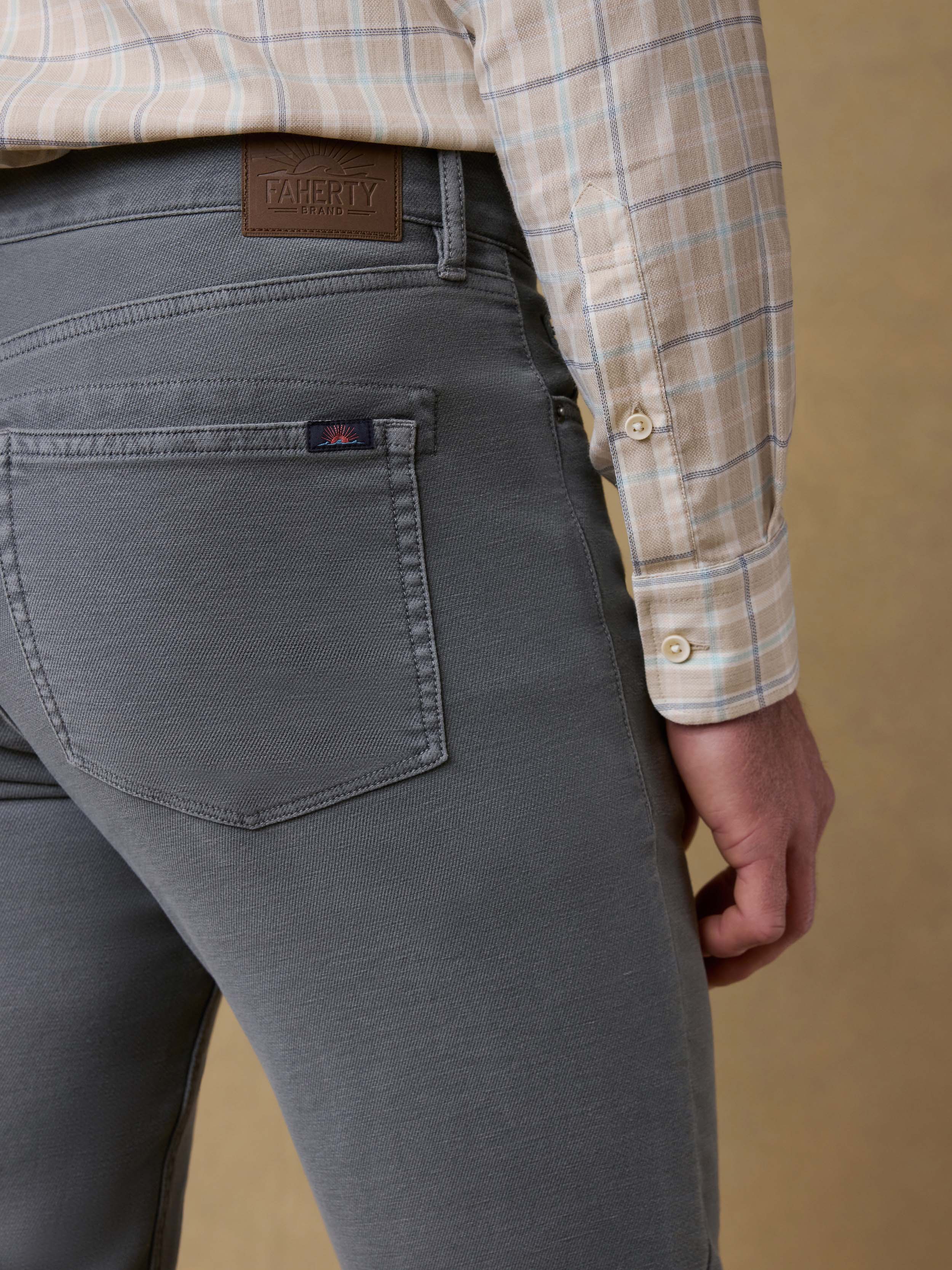 Detail back view of a man wearing a plaid button up shirt with gray pants against a beige background