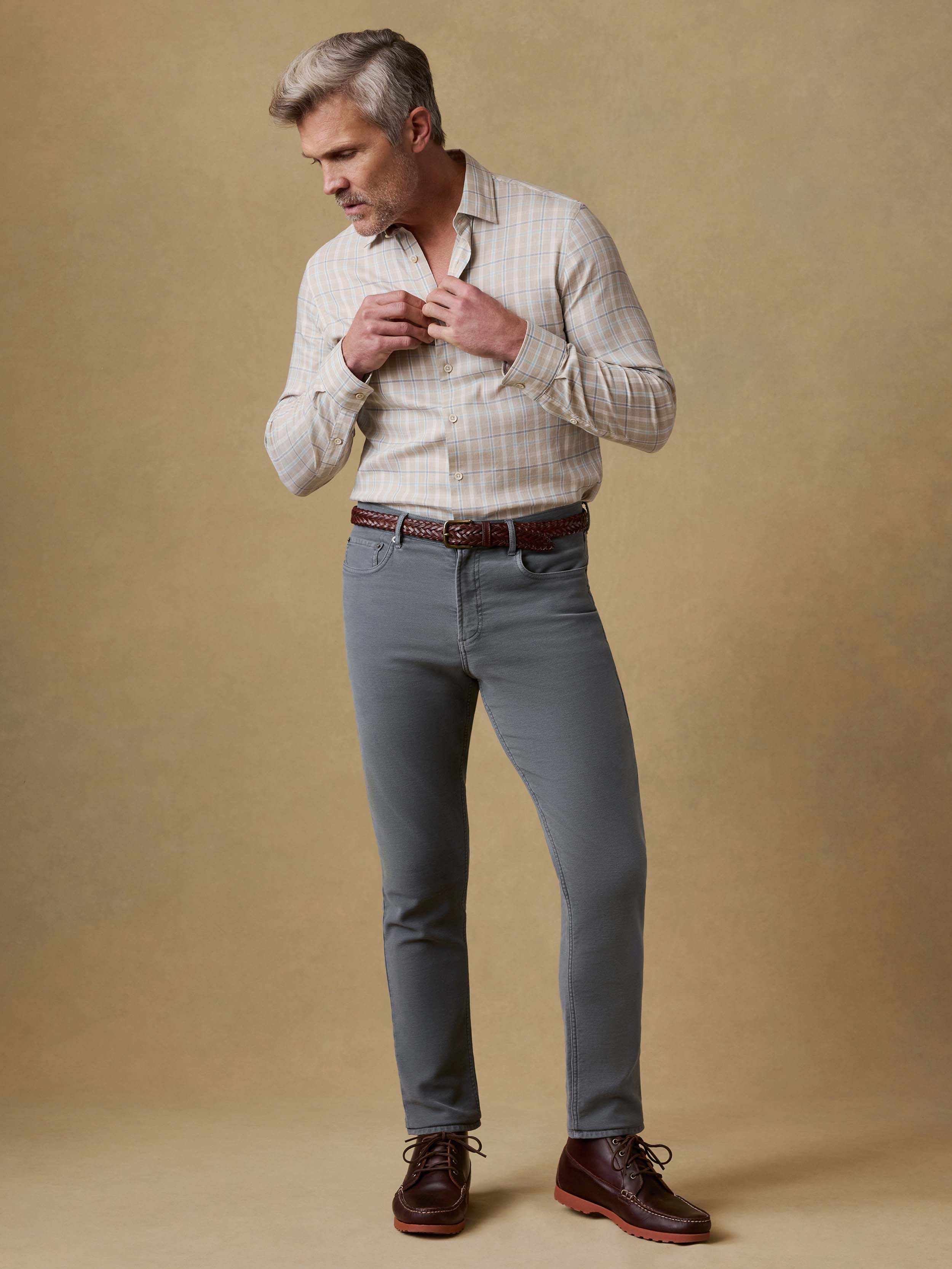 Man is wearing a plaid button up shirt with gray pants against a beige background