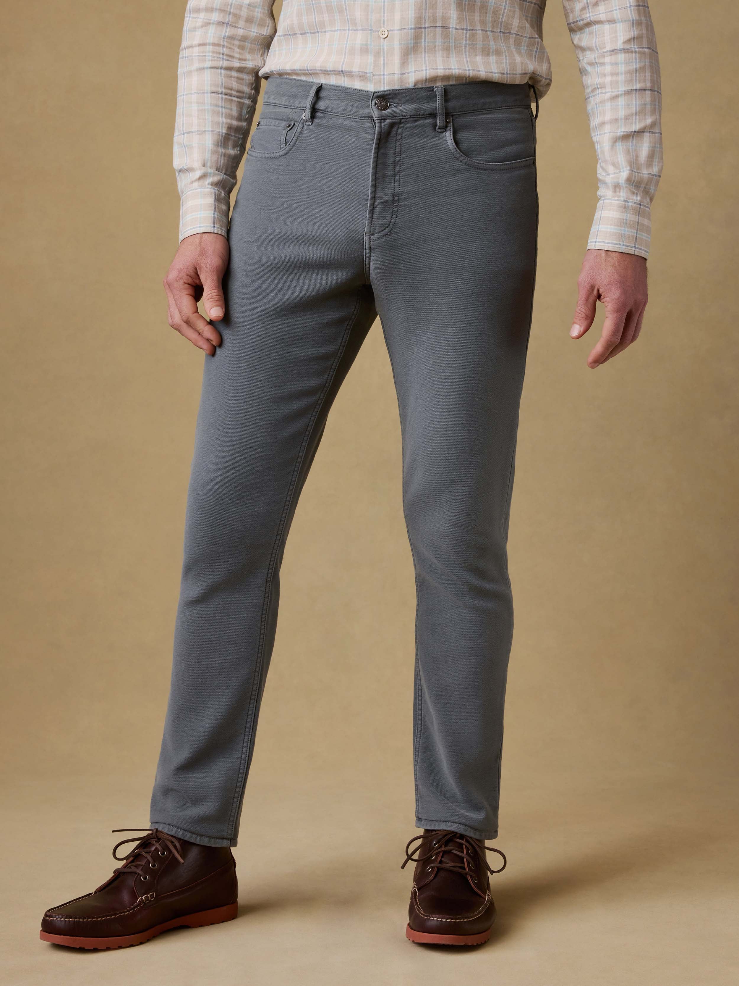 Man is wearing a plaid button up shirt with gray pants against a beige background