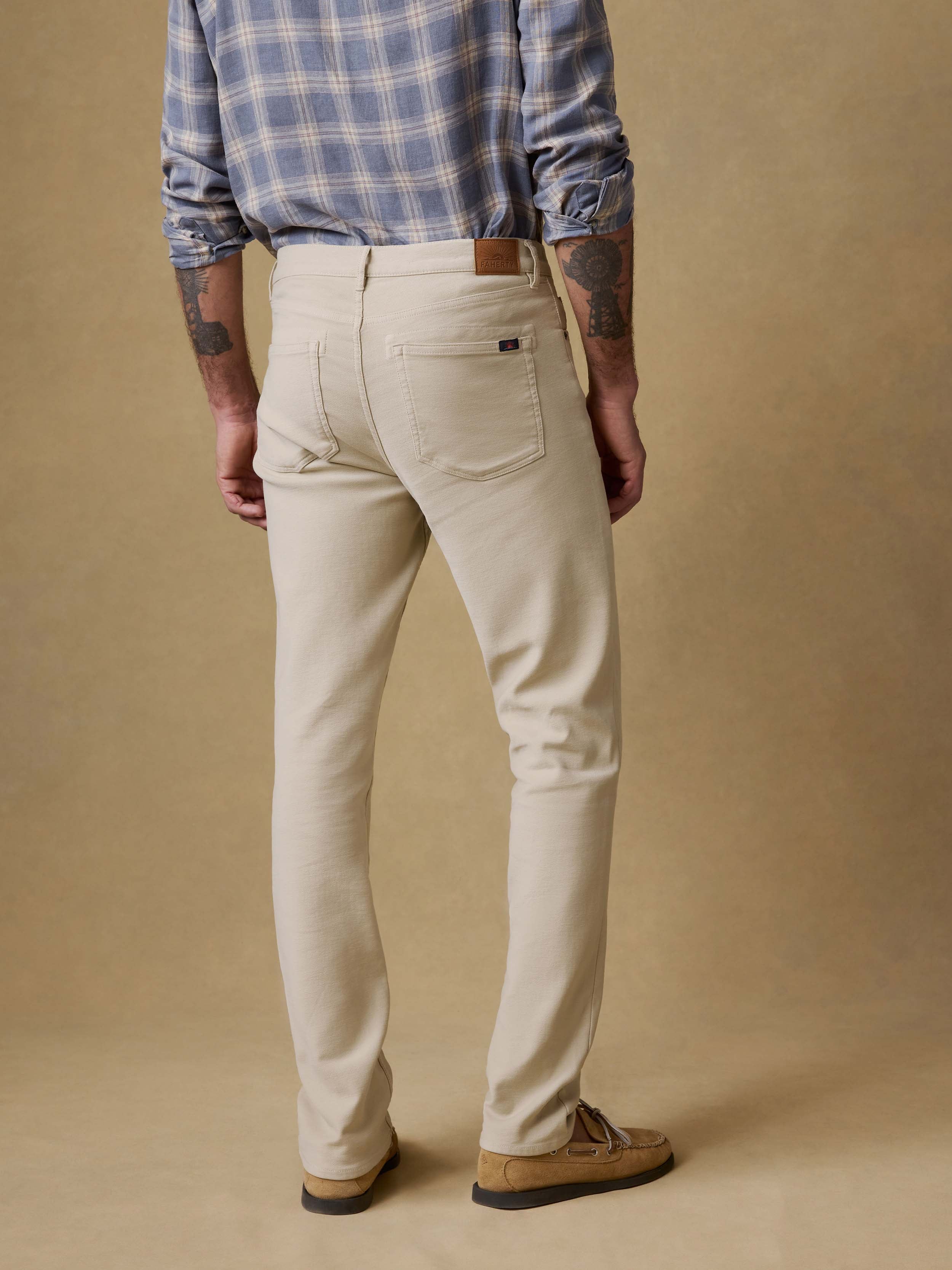 Back view of a man wearing a blue plaid shirt and beige pants against a beige background