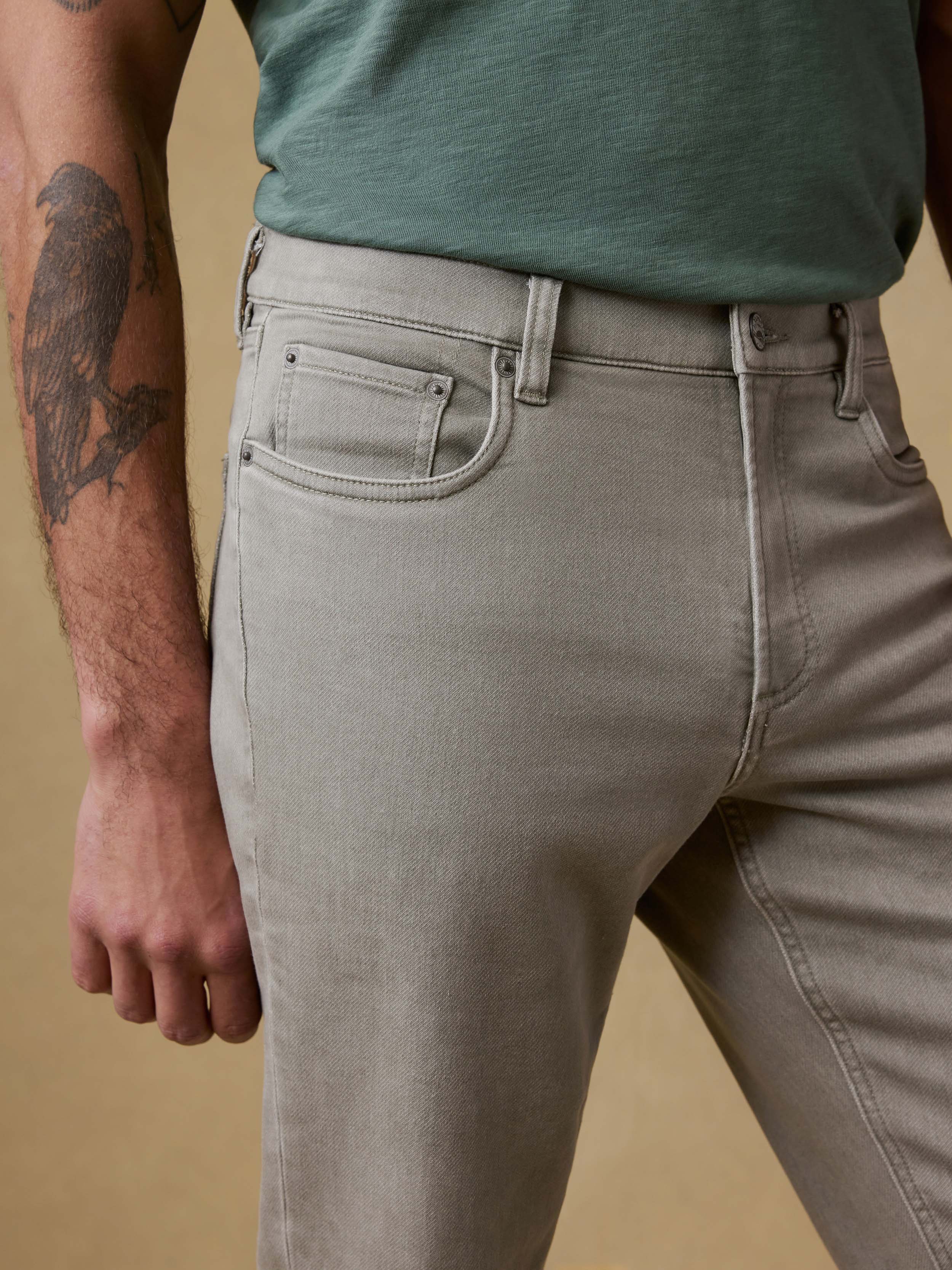 Detail front view of a man wearing light green pants and a green t-shirt against a beige background
