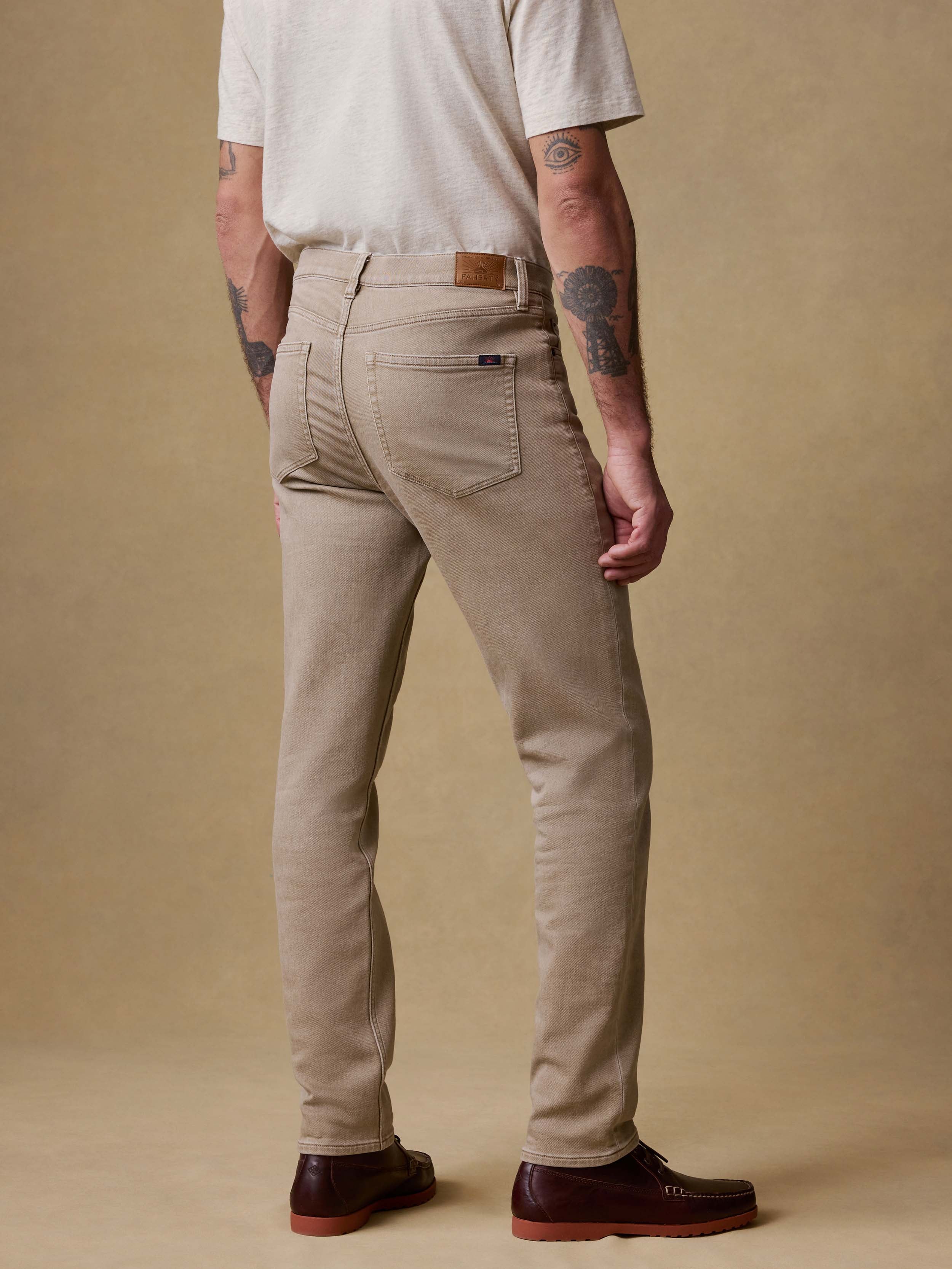 Back view of a man wearing beige pants and a white shirt against a brown background