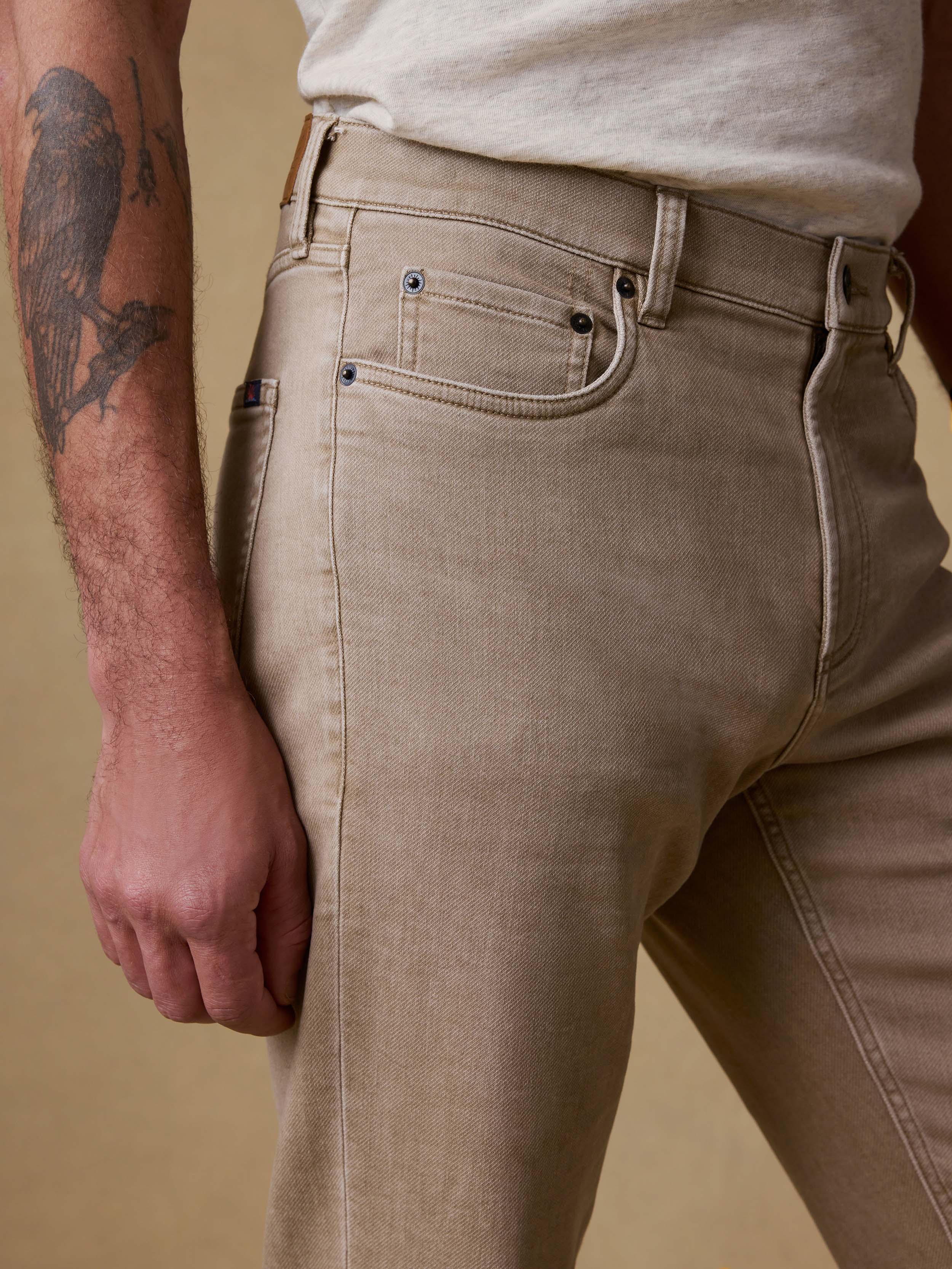 Detail front view of a man wearing beige pants and a white shirt against a brown background