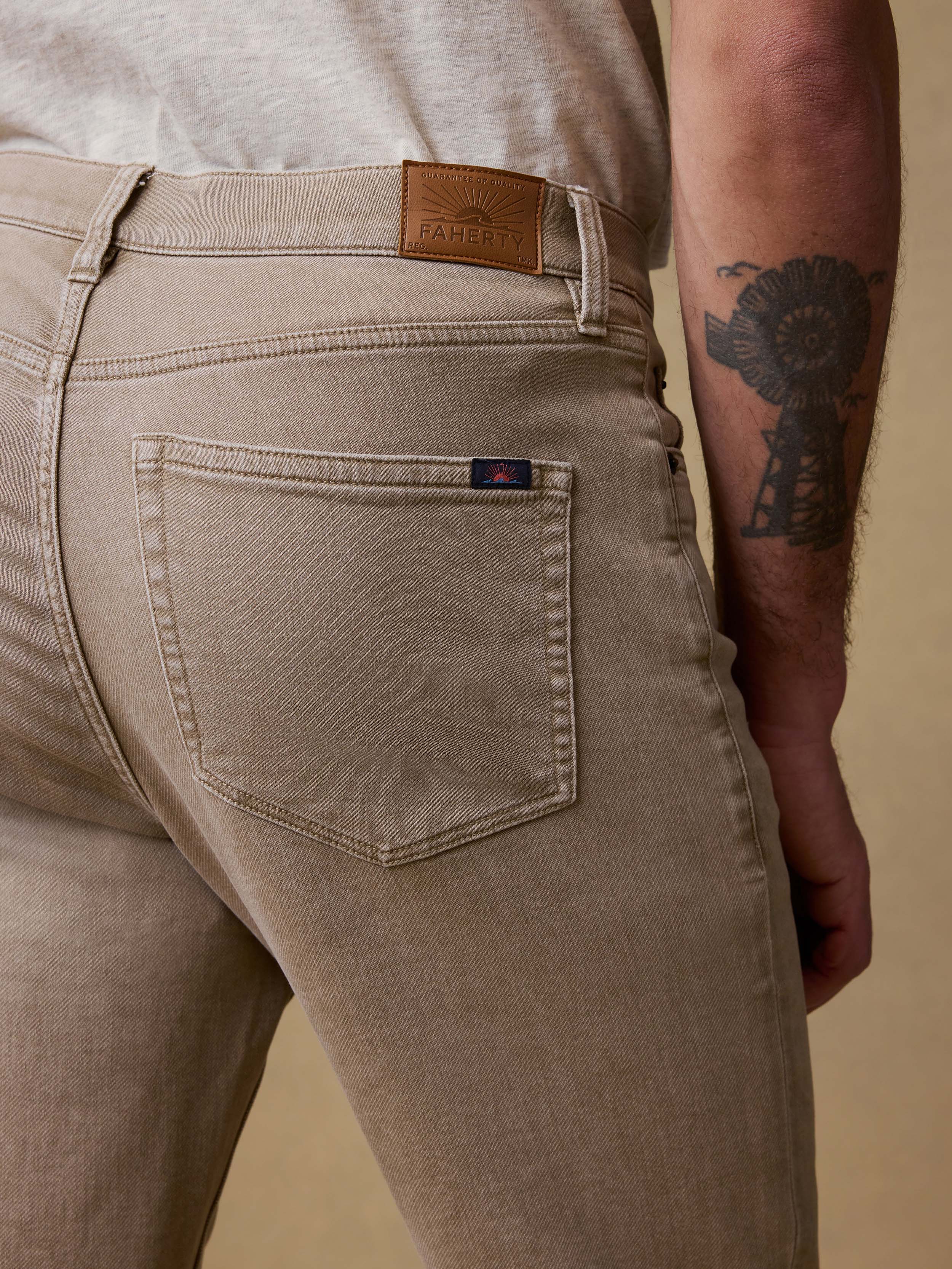 Detail back view of a man wearing beige pants and a white shirt against a brown background