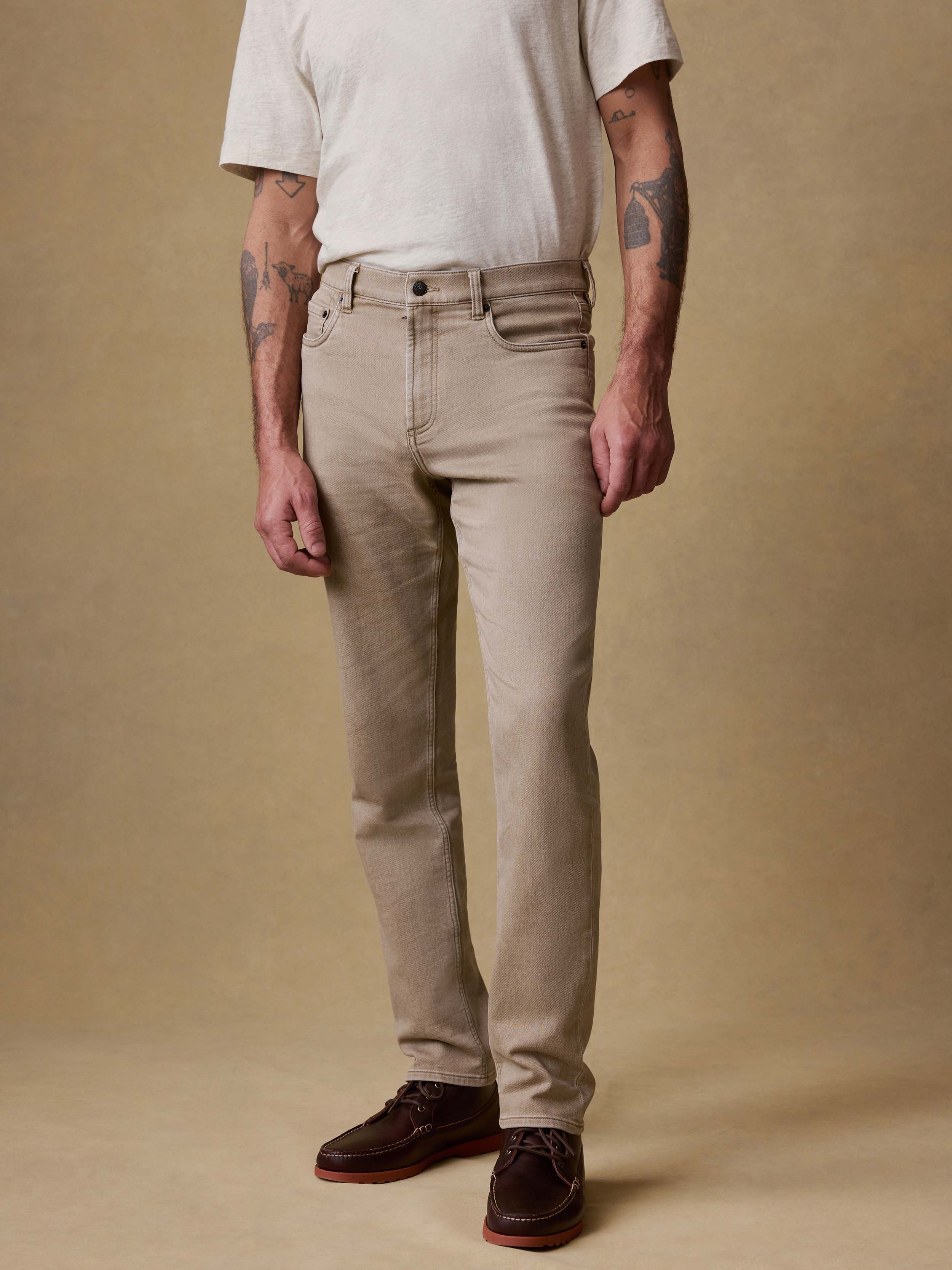 Man wearing beige pants and a white shirt against a brown background