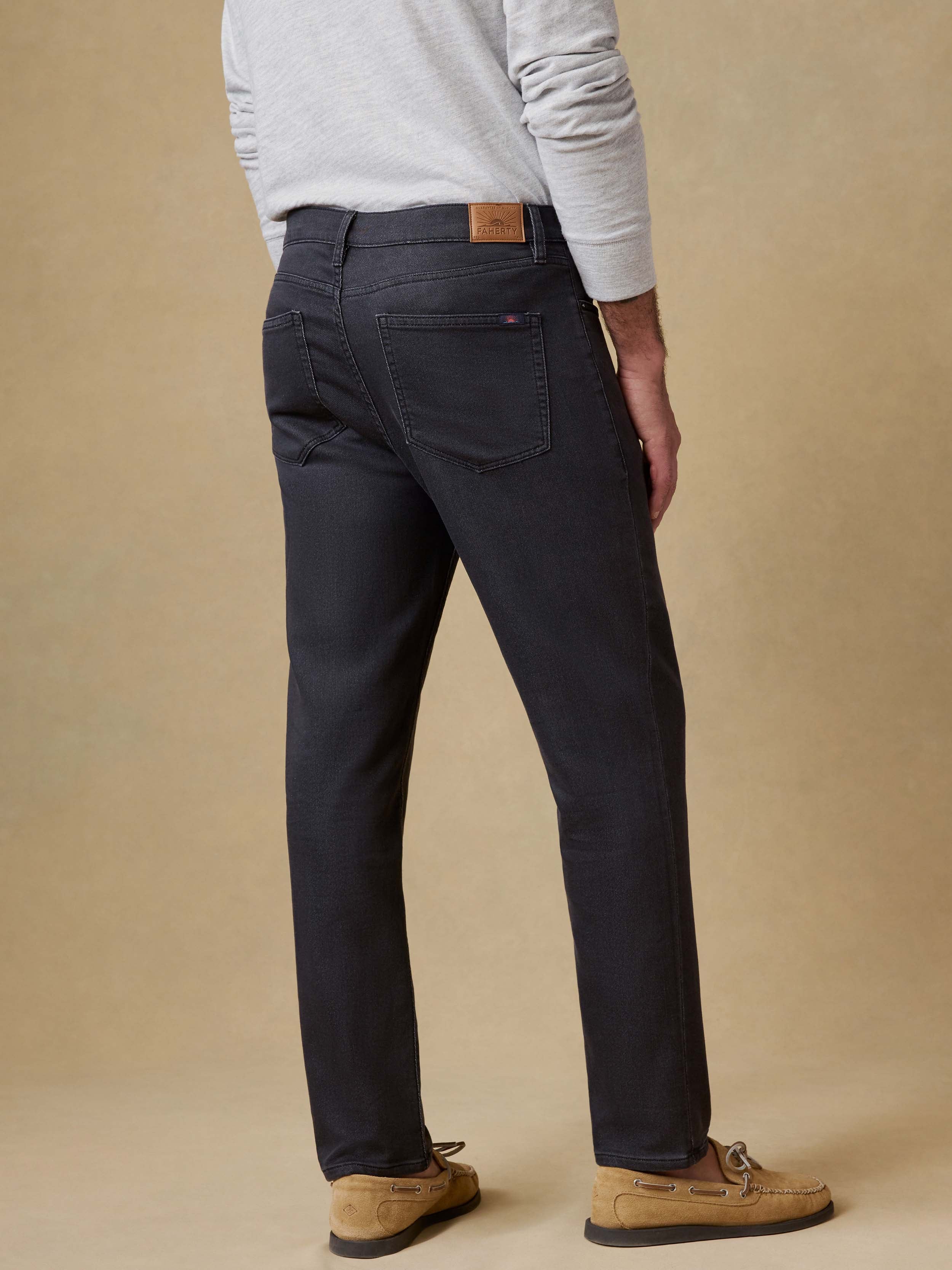 Back view of a man wearing black jeans and a gray sweater against a beige background