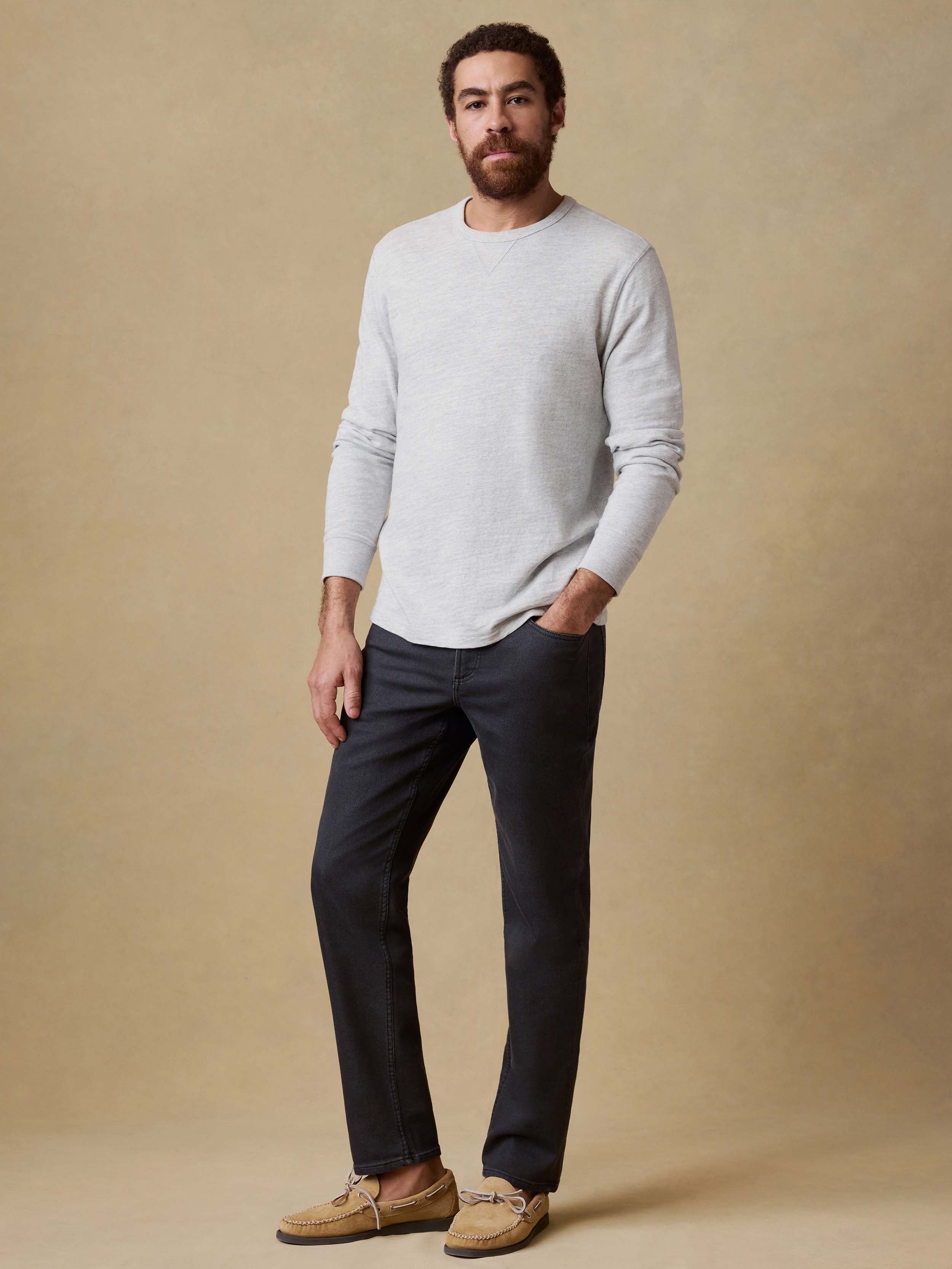 Man wearing black jeans and a gray sweater against a beige background