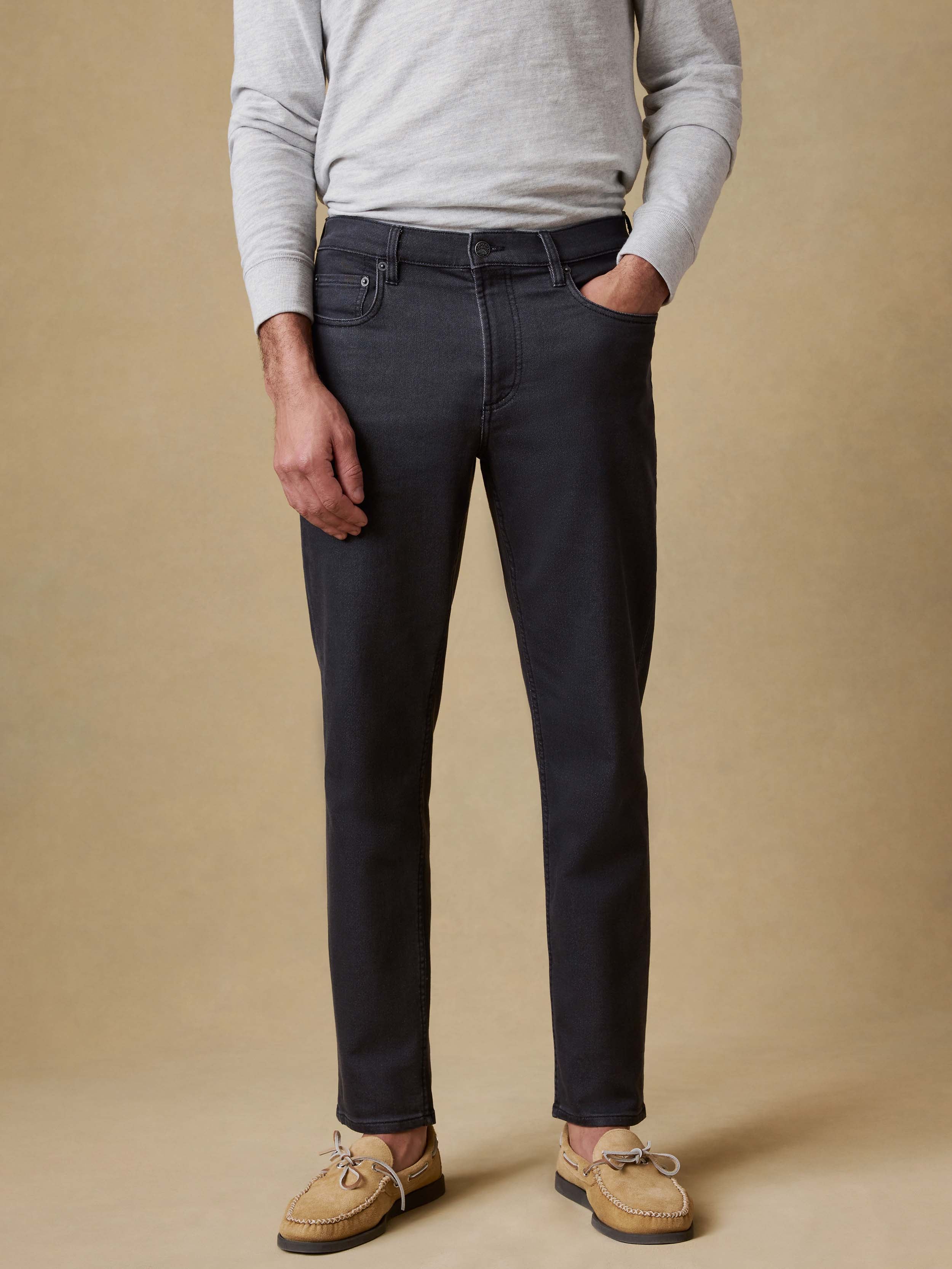 Man wearing black jeans and a gray sweater against a beige background