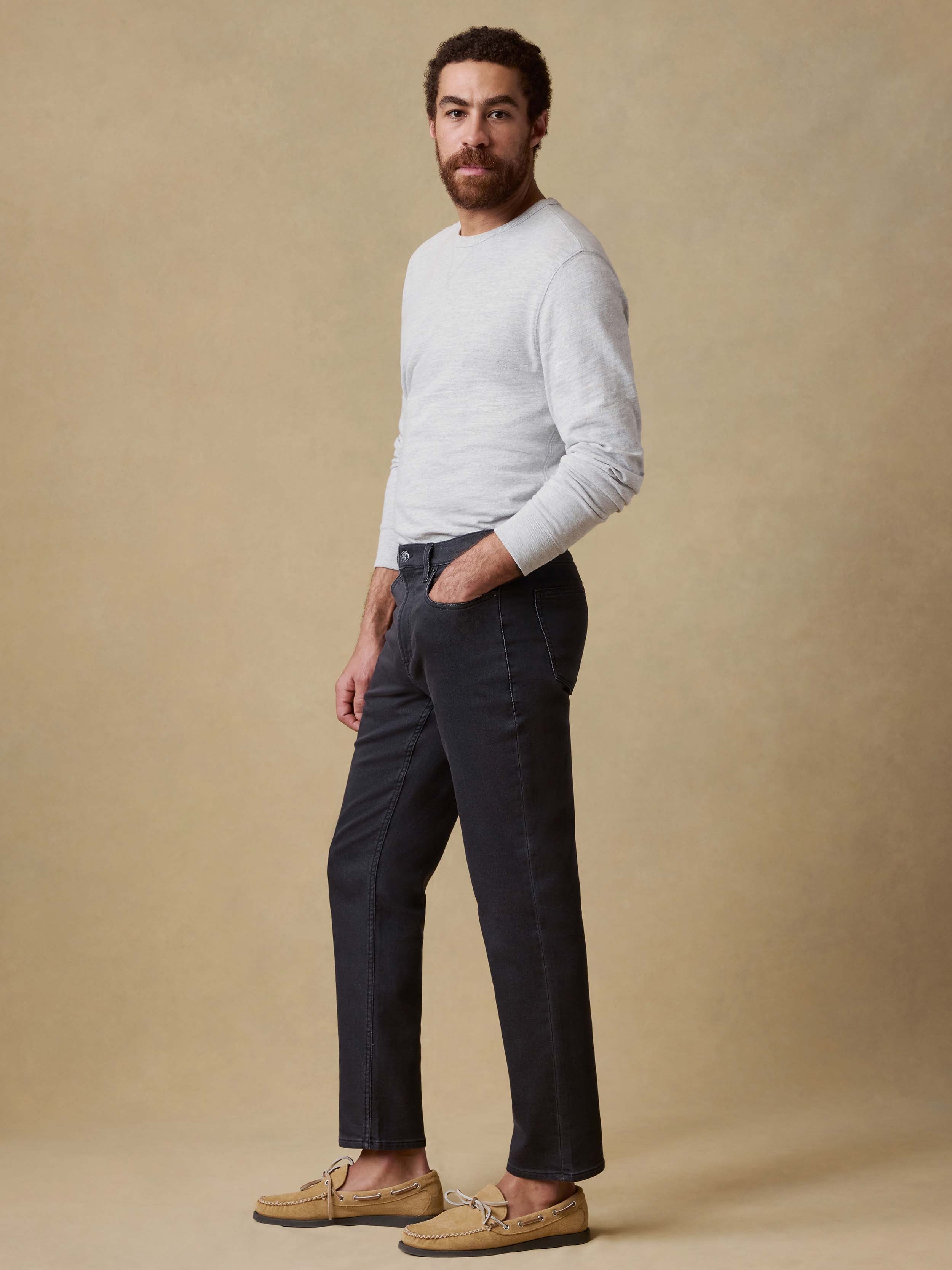 Man wearing black jeans and a gray sweater against a beige background