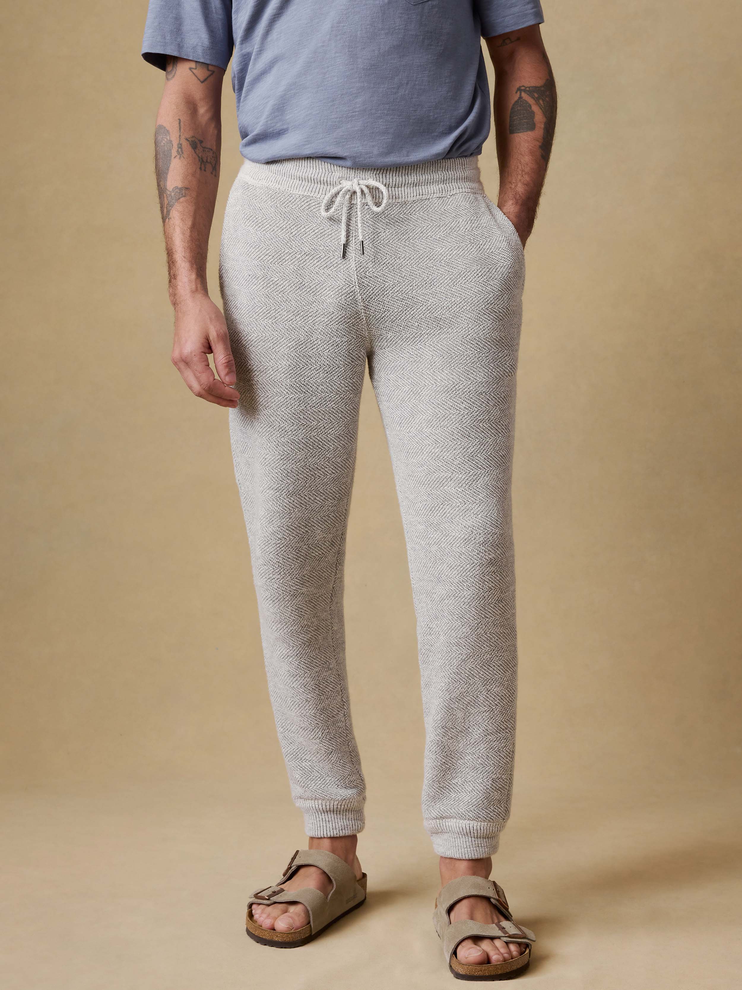 Man wearing gray jogger sweatpants and a blue t-shirt on a beige background