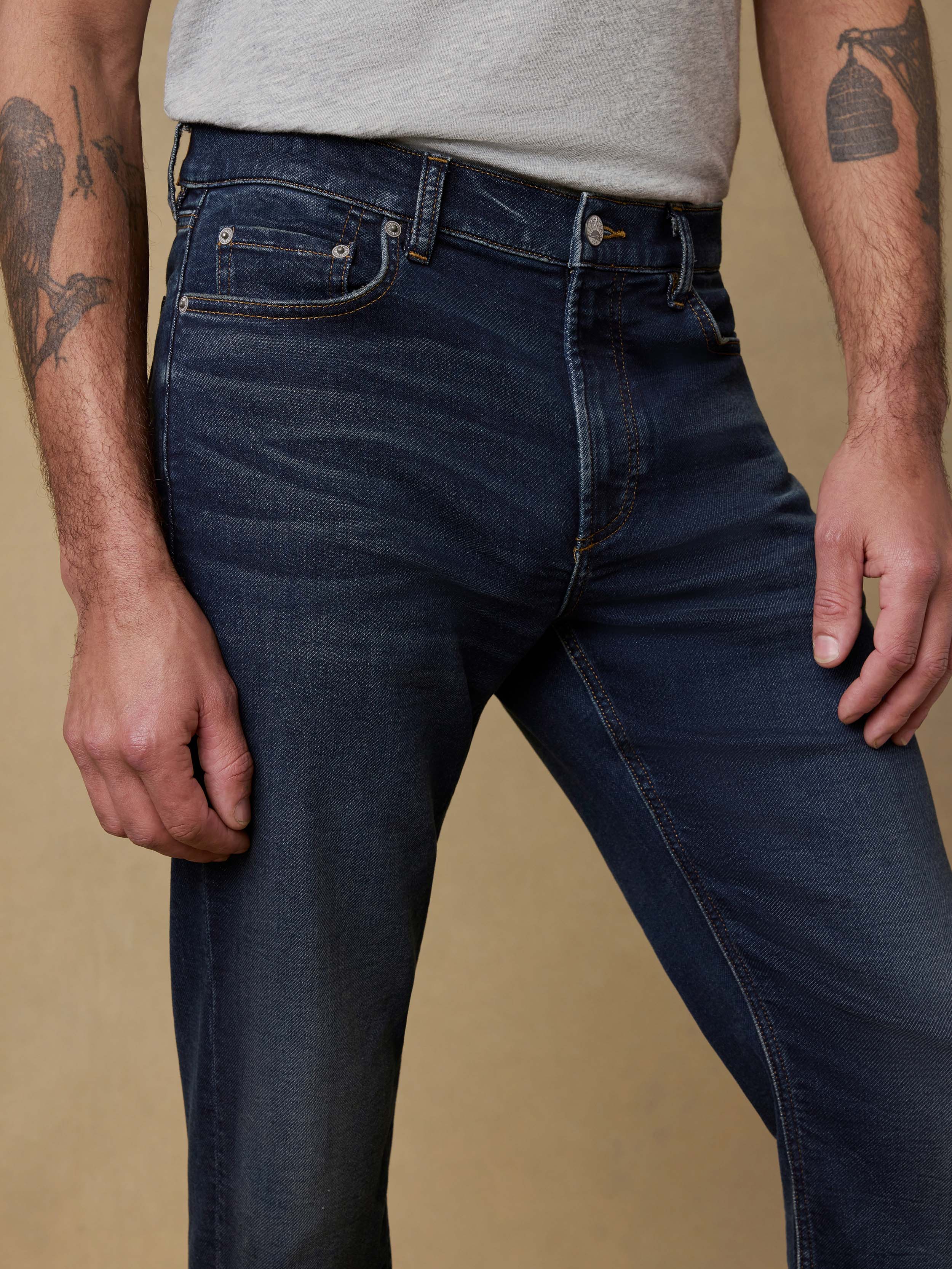 Detail front view of a man wearing a gray t-shirt and dark blue jeans against a beige background