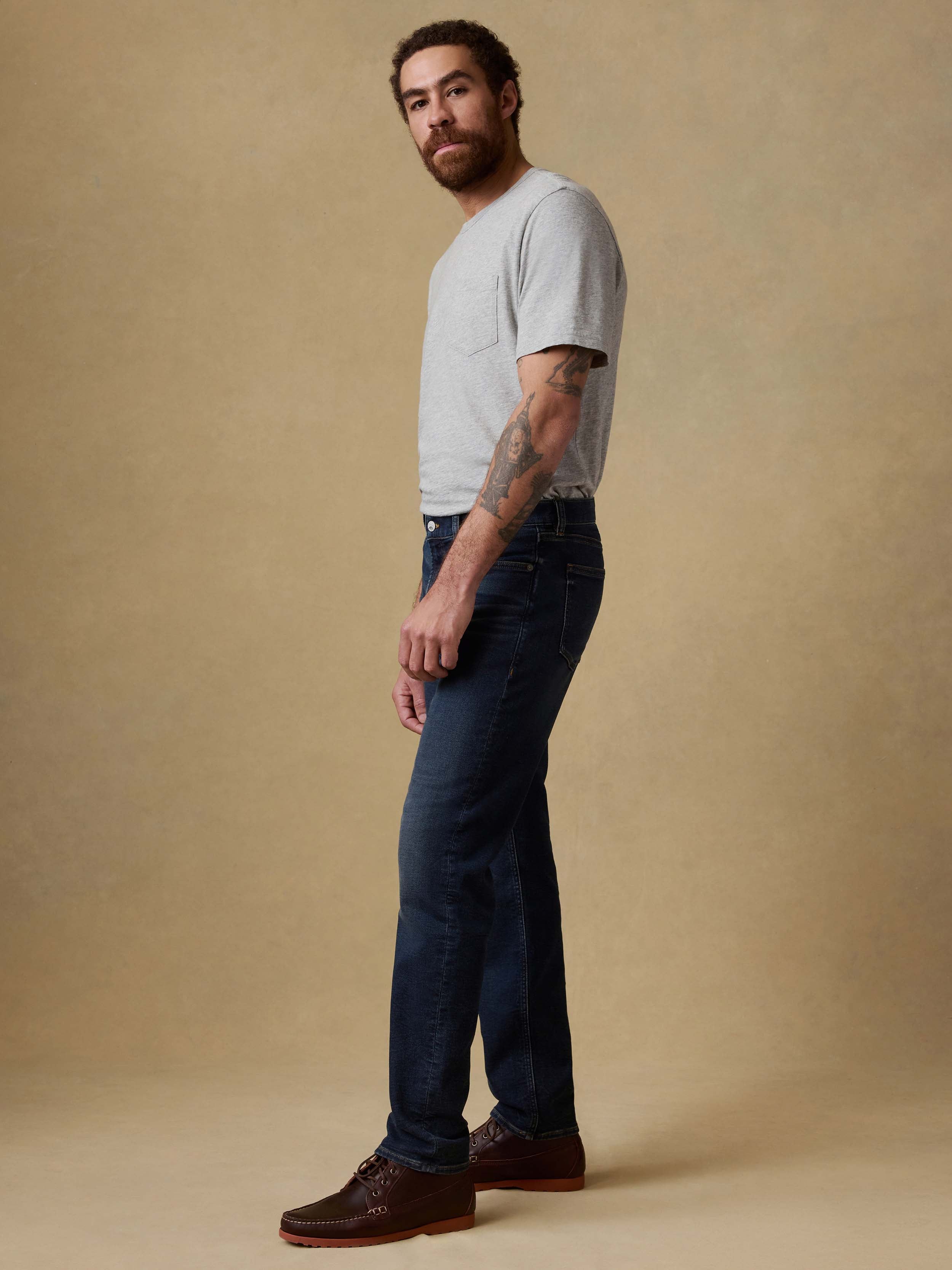 Man wearing a gray t-shirt and dark blue jeans against a beige background