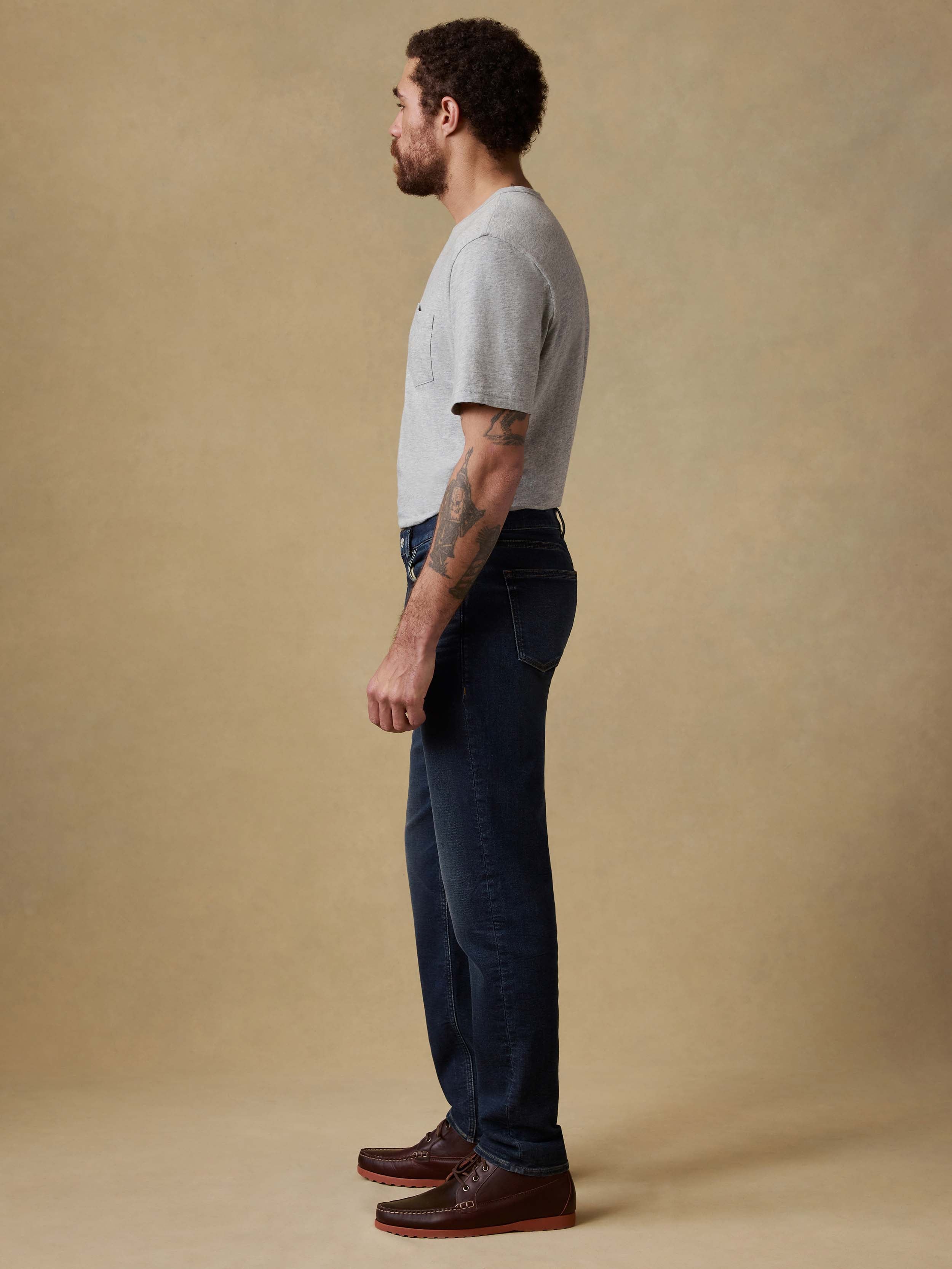 Man wearing a gray t-shirt and dark blue jeans against a beige background
