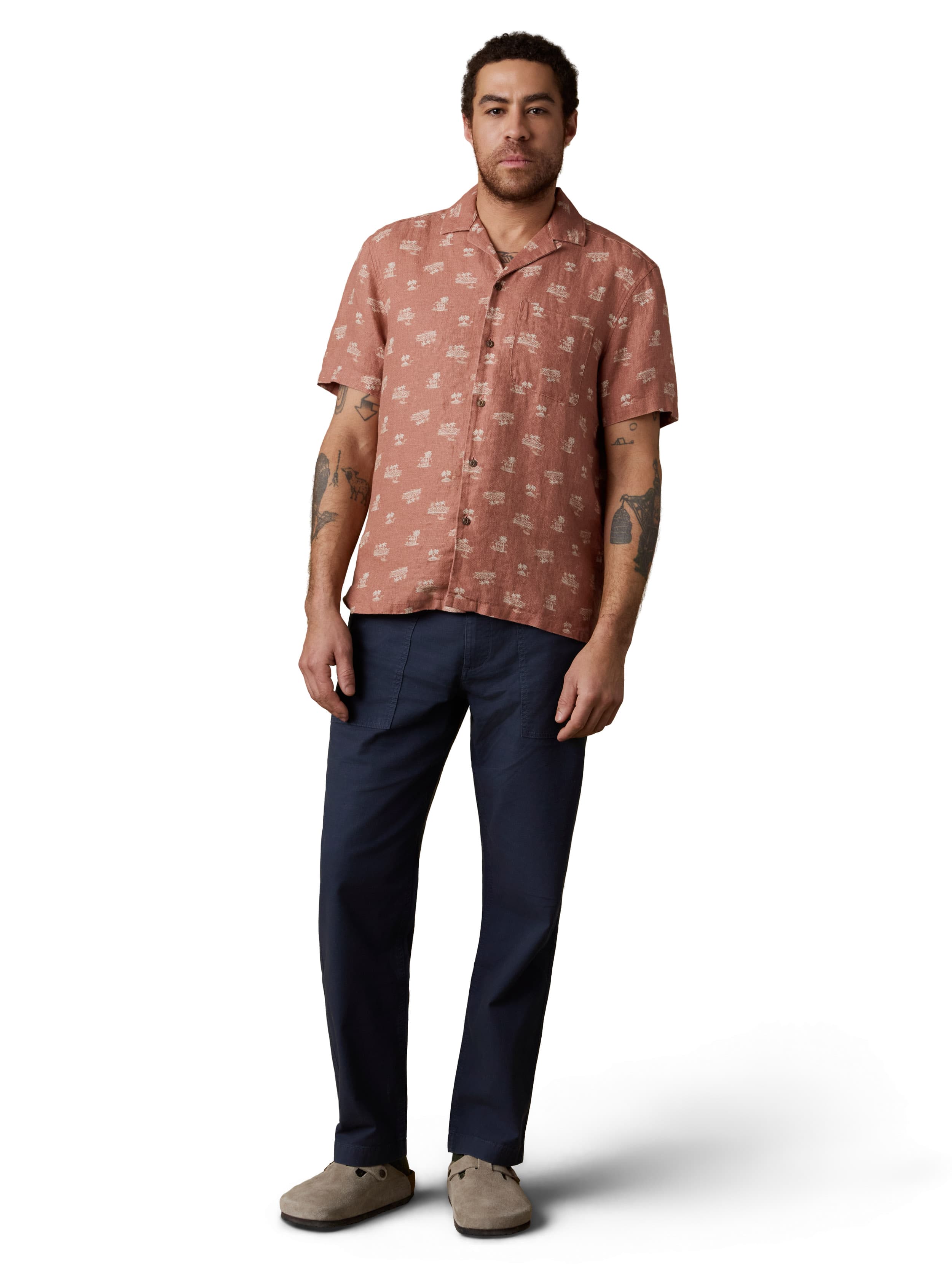 A man wearing an orange button up shirt, blue pants, and birkenstocks