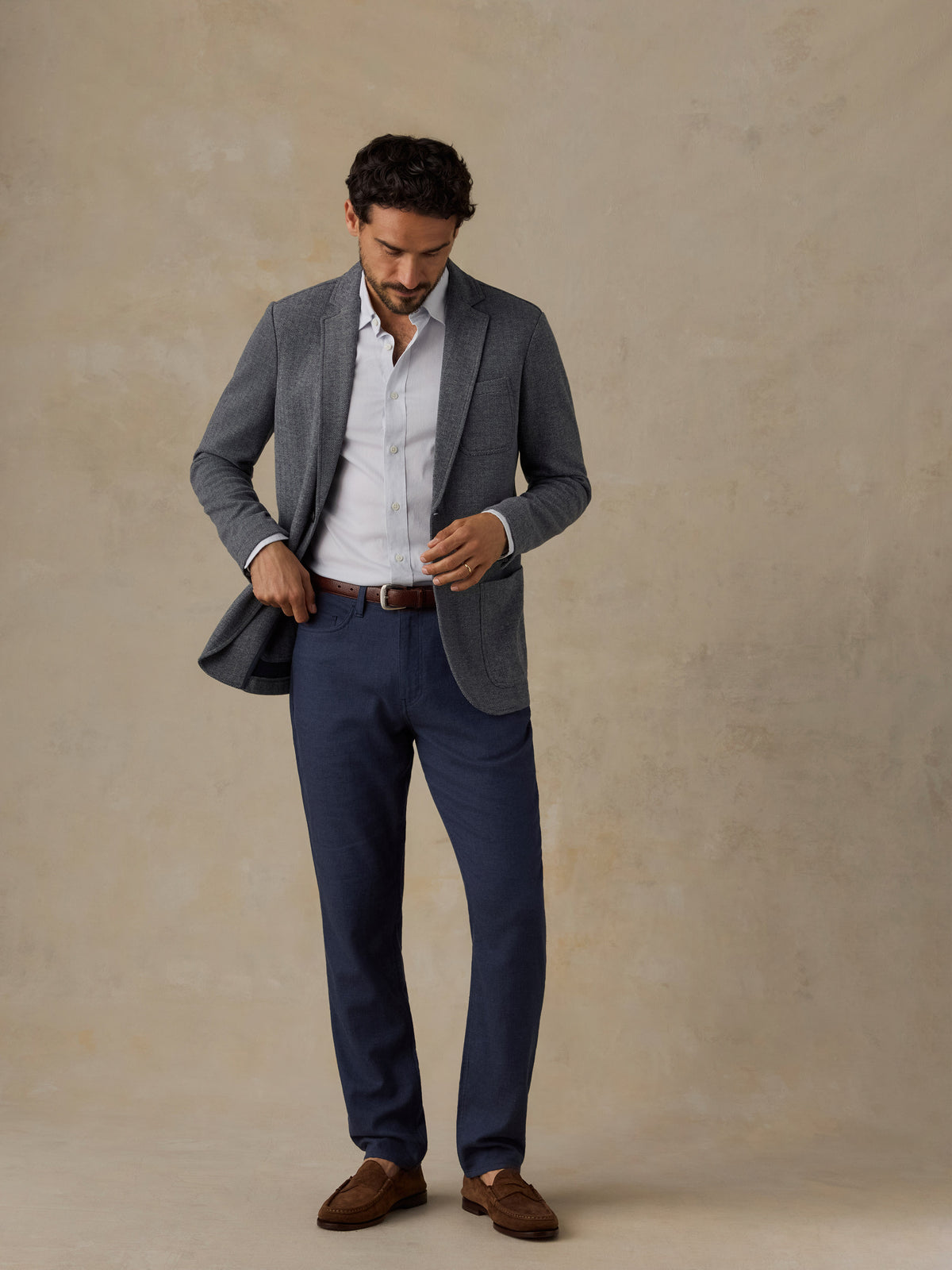 Man wearing a grey blazer and navy pants against a beige background, image 4 of 5