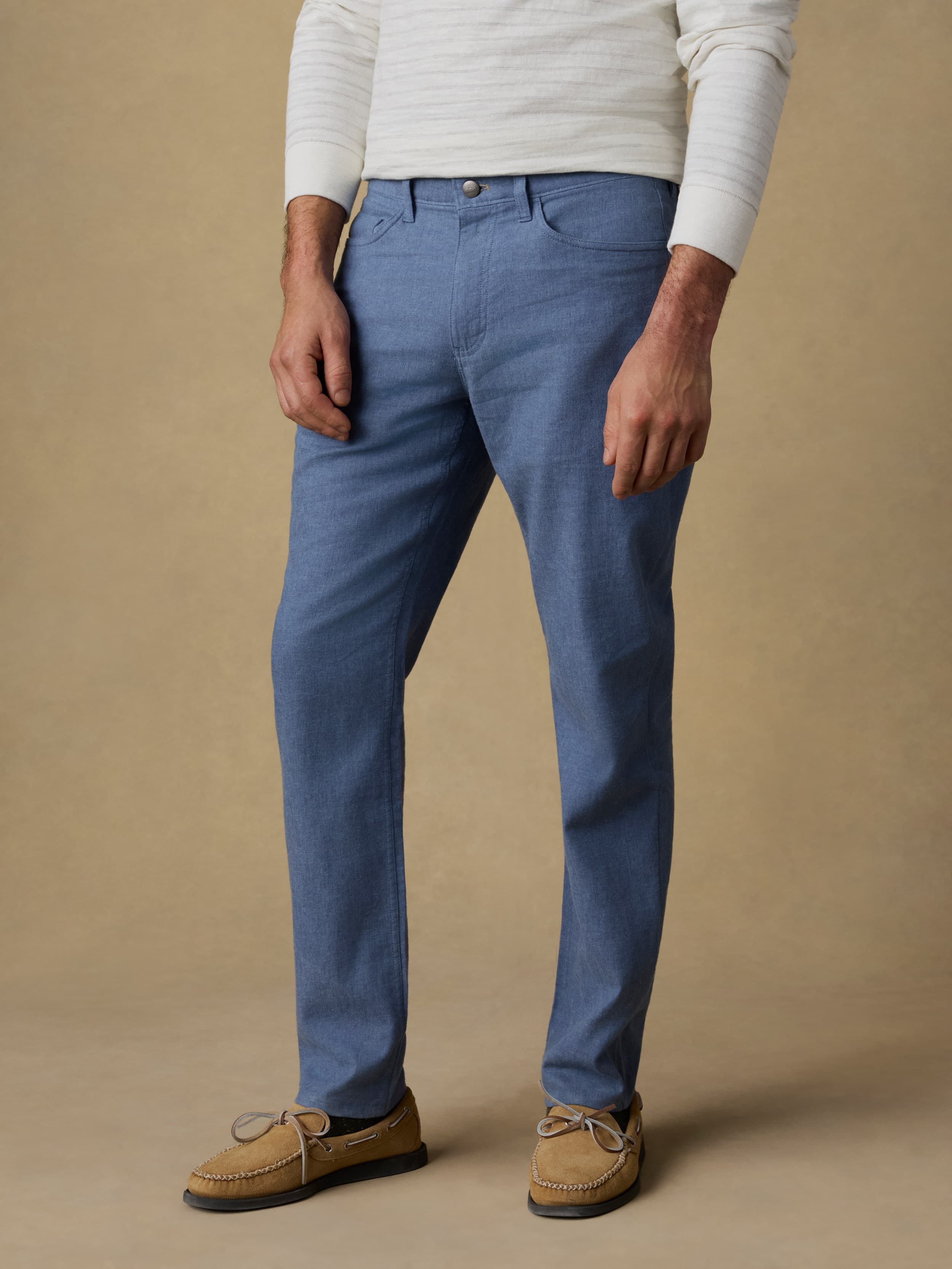 Man wearing a white and grey striped long sleeve t-shirt with blue linen pants against a beige background