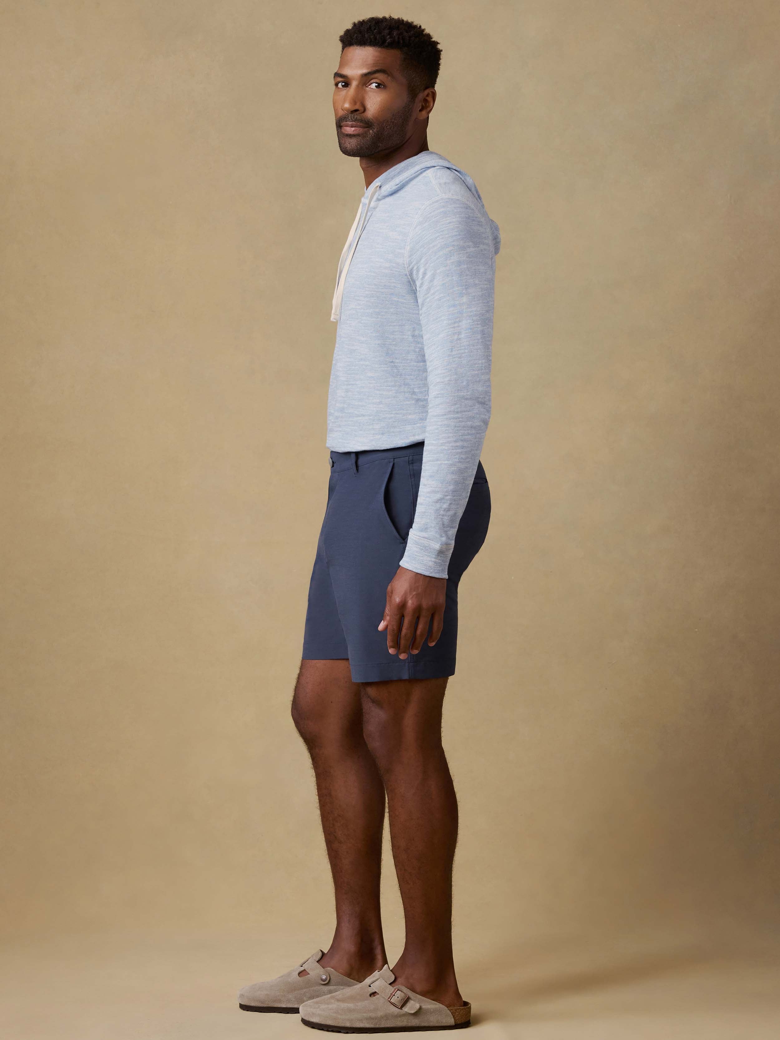 Man wearing a light blue hoodie and navy shorts against a beige background