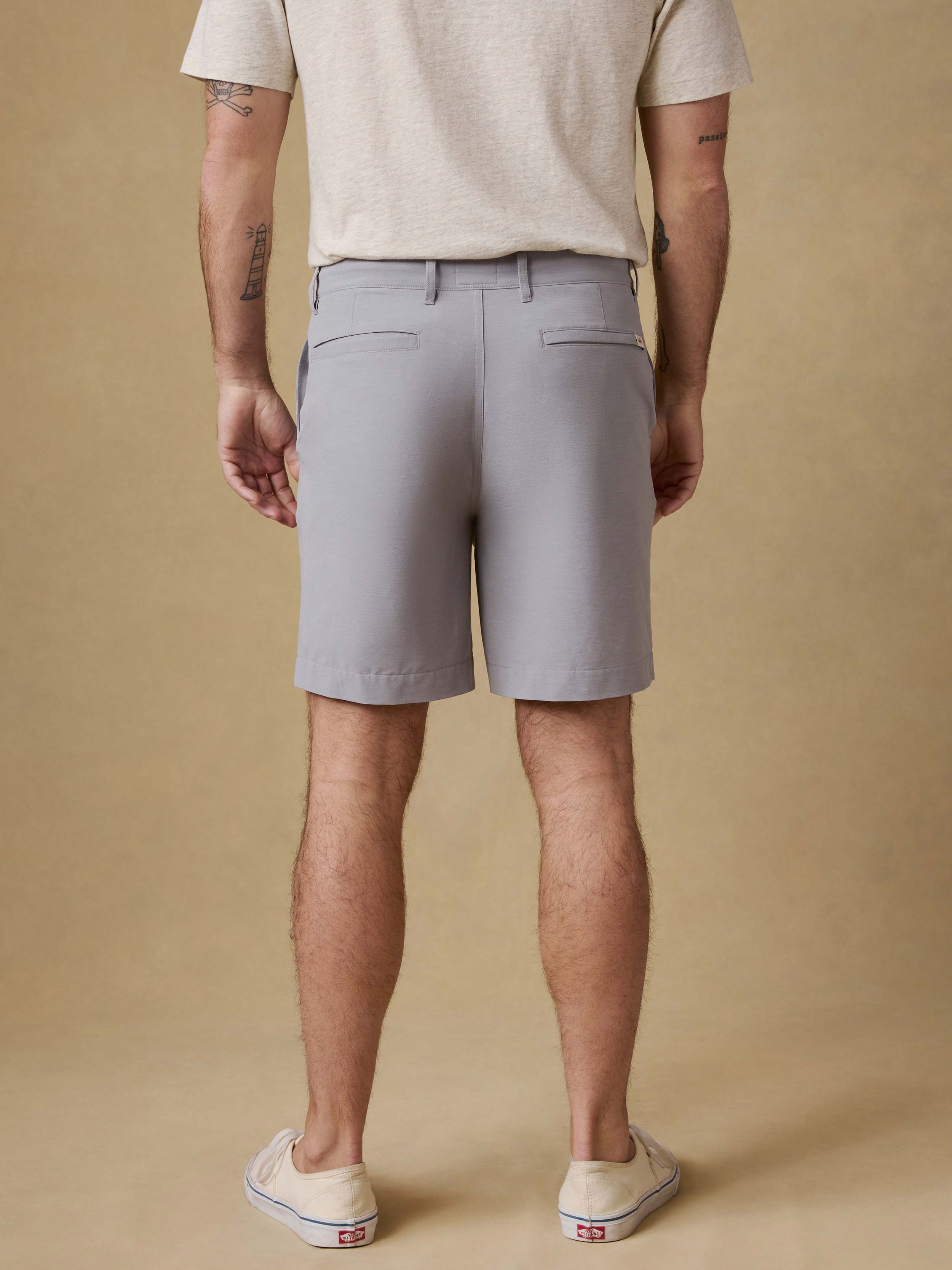 Back view of a man wearing gray shorts and a light gray t-shirt on a beige background