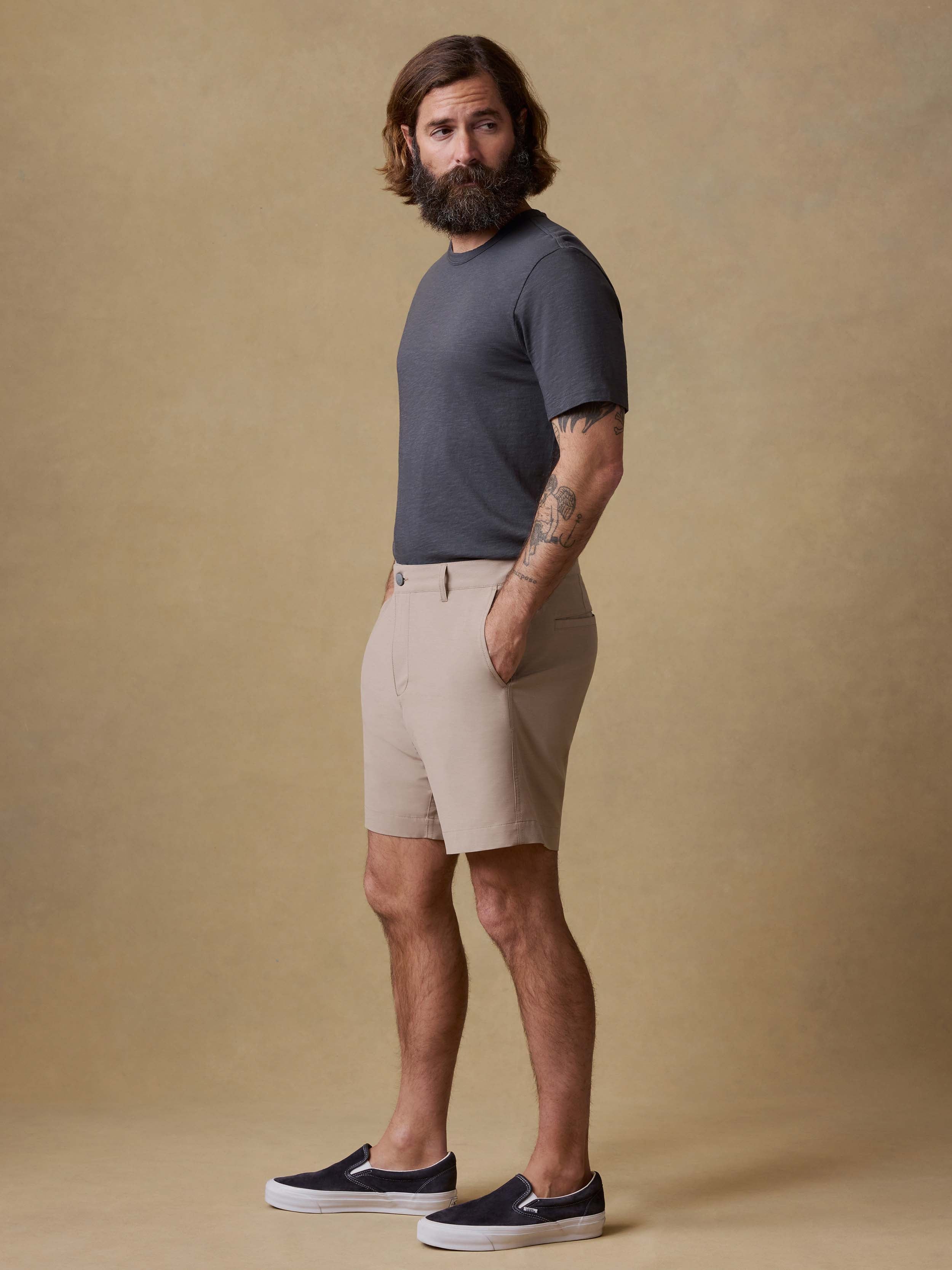 Man wearing a dark gray t-shirt and beige shorts against a beige background