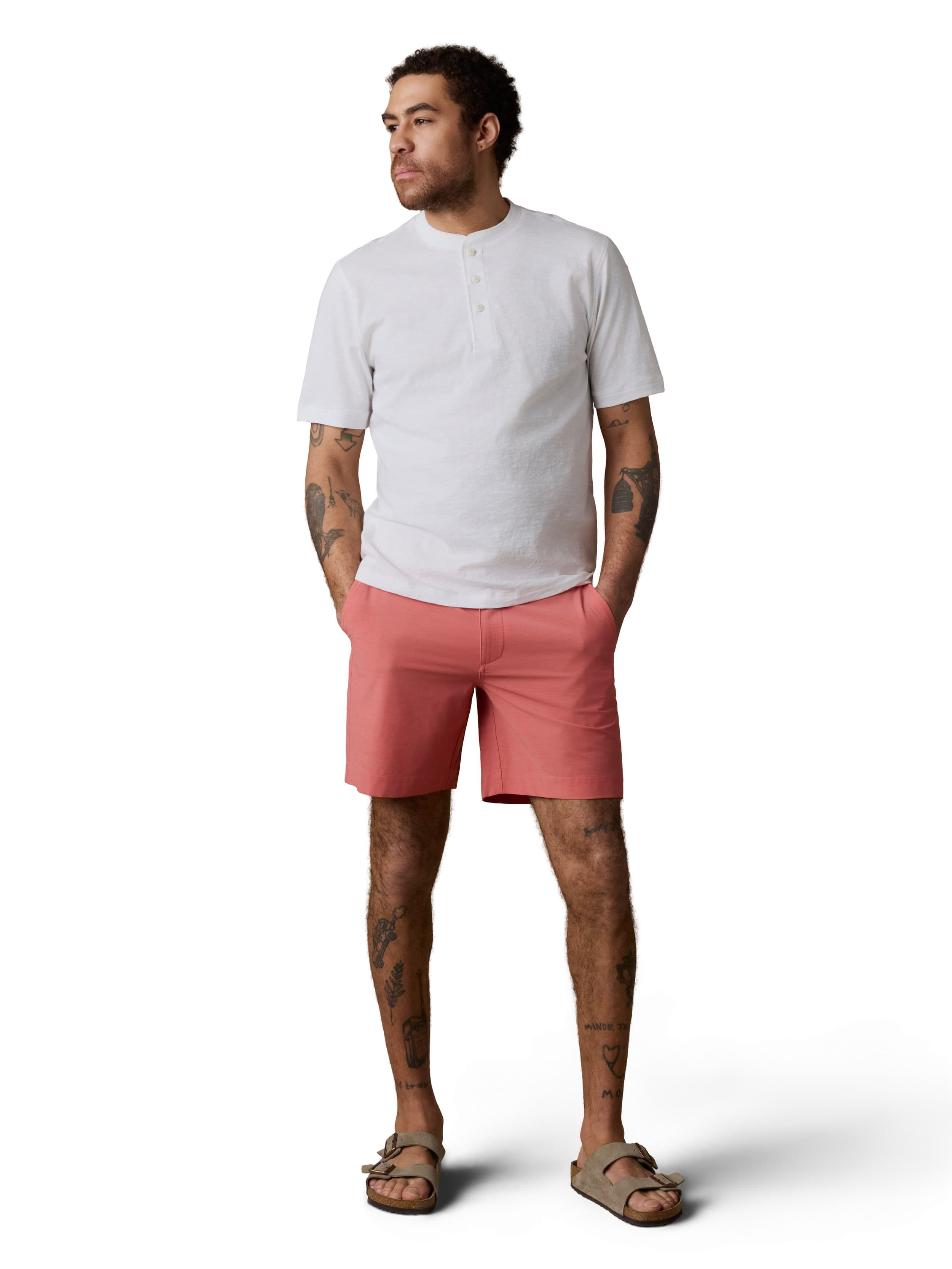 A man wearing a white henley tee, coral shorts, and birkenstocks