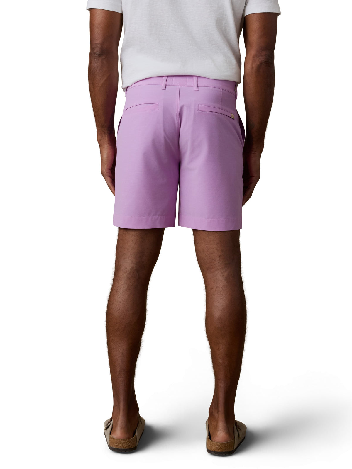 A man viewed from the back wearing a white tee, purple shorts, and birkenstocks, image 2 of 2
