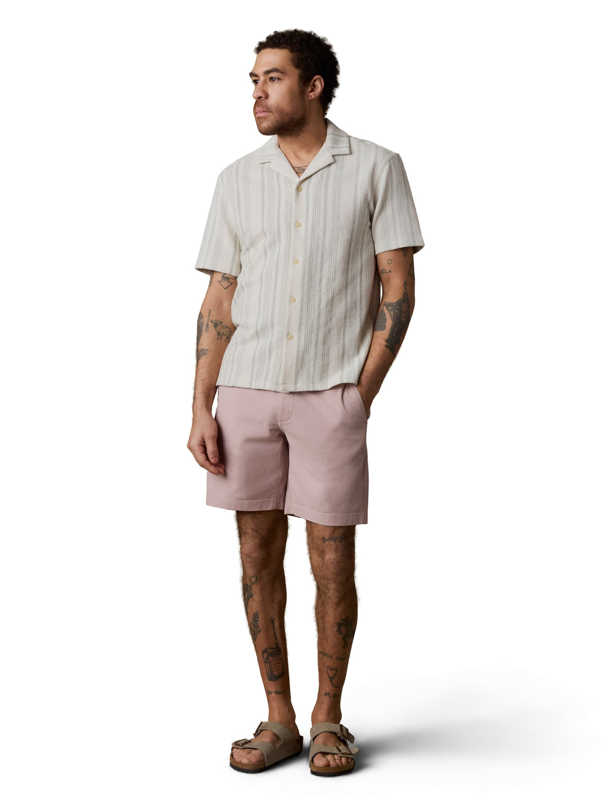 A man wearing a white striped button up shirt, pink pants, and birkenstocks, image 1 of 4