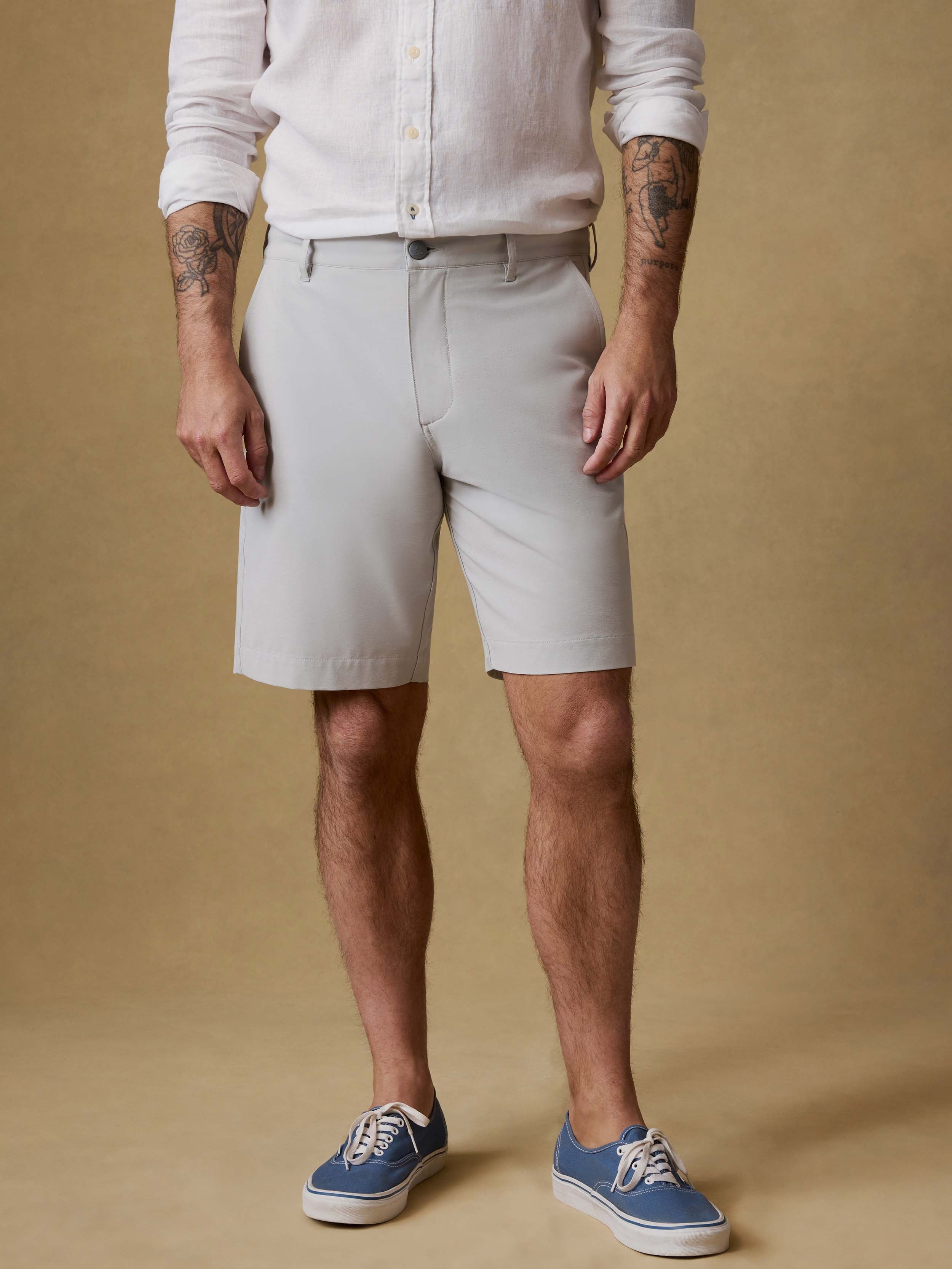 Man wearing light gray shorts and blue sneakers on a beige background