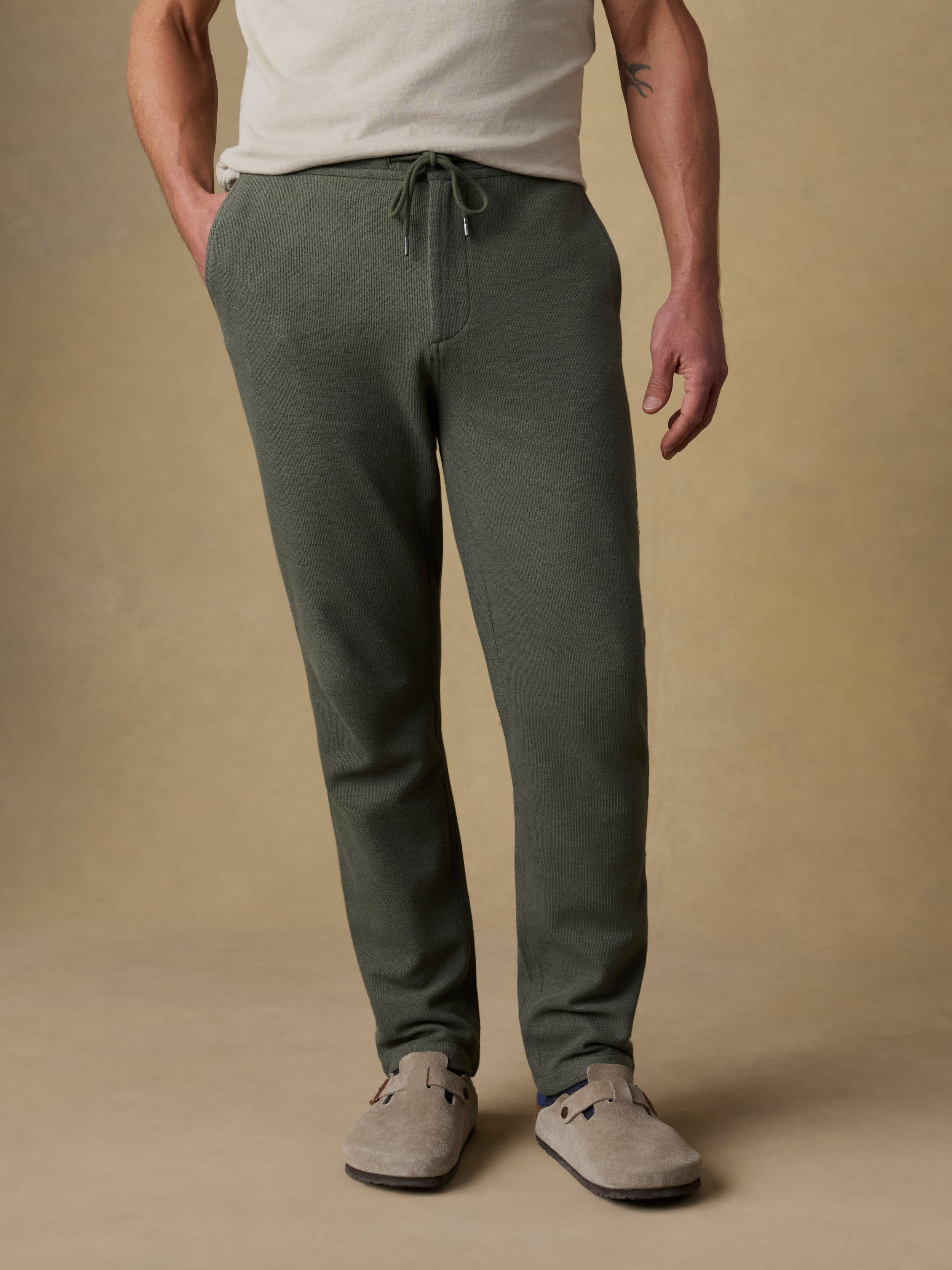 Man wearing a beige t-shirt with green sweatpants against a beige background