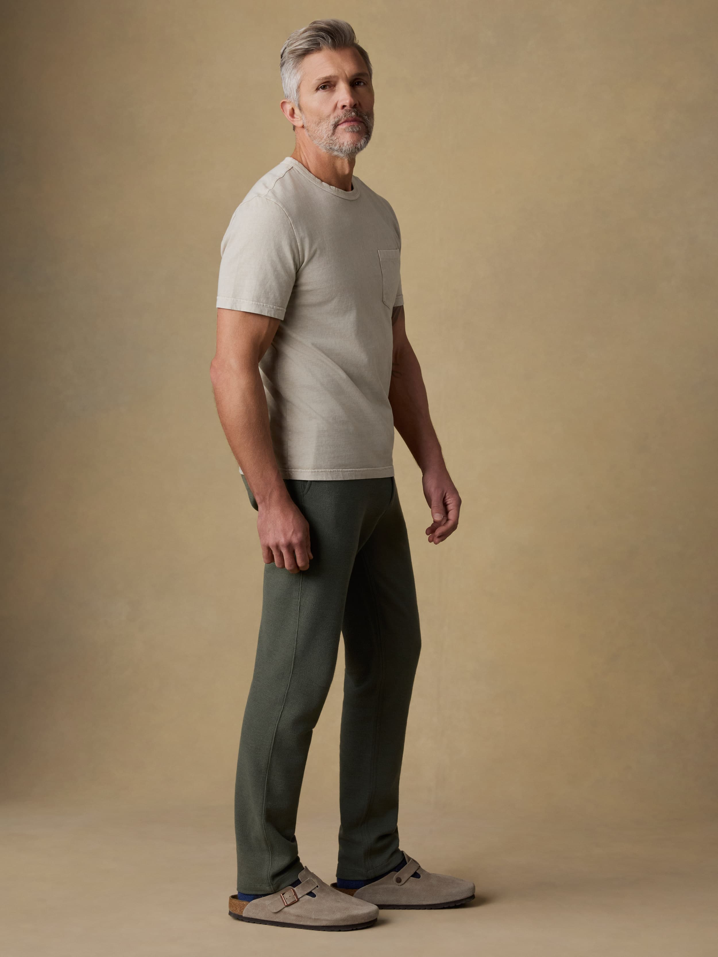 Man wearing a beige t-shirt with green sweatpants against a beige background