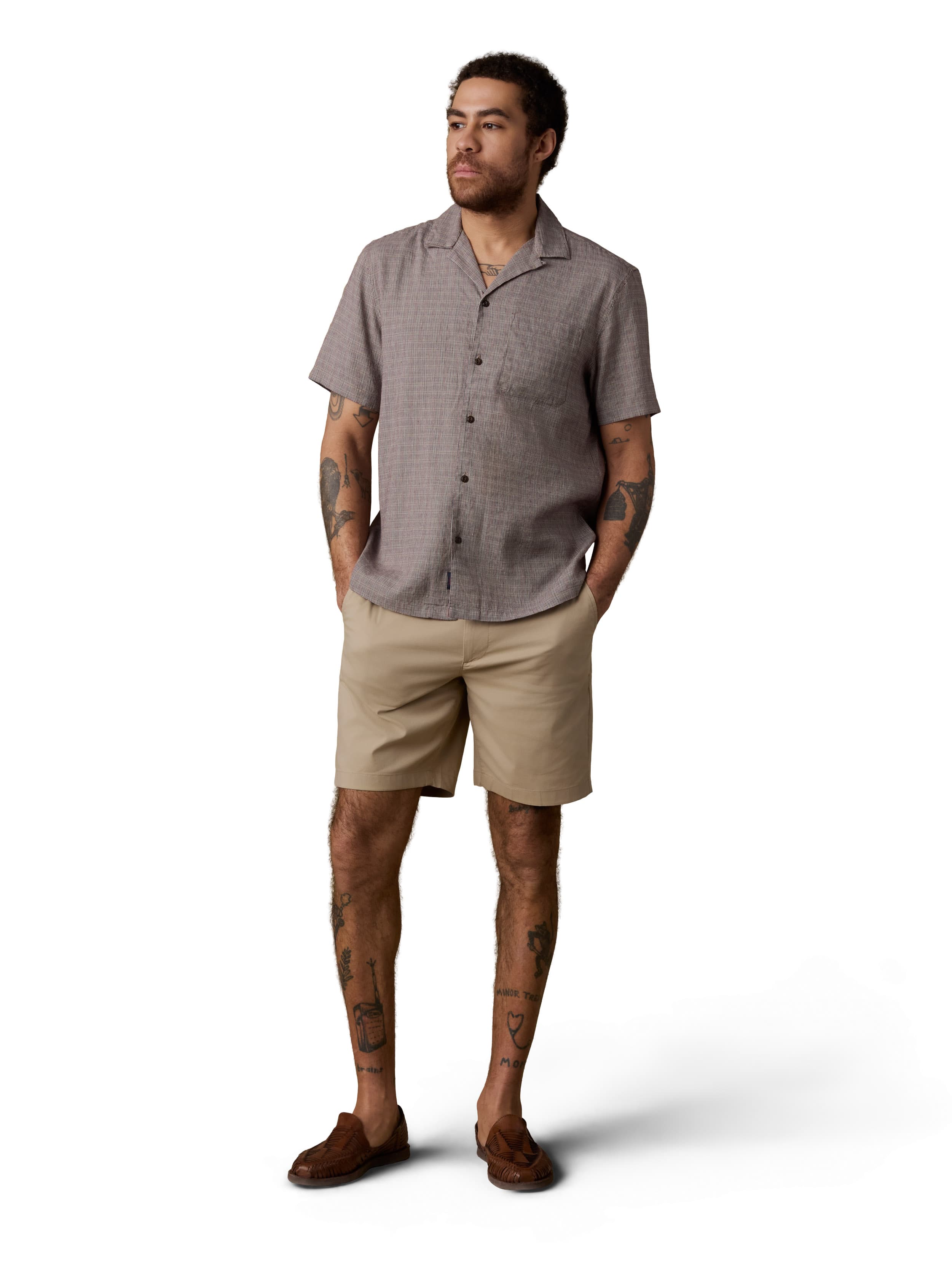 A man wearing a brown button up shirt, beige shorts, and brown shoes