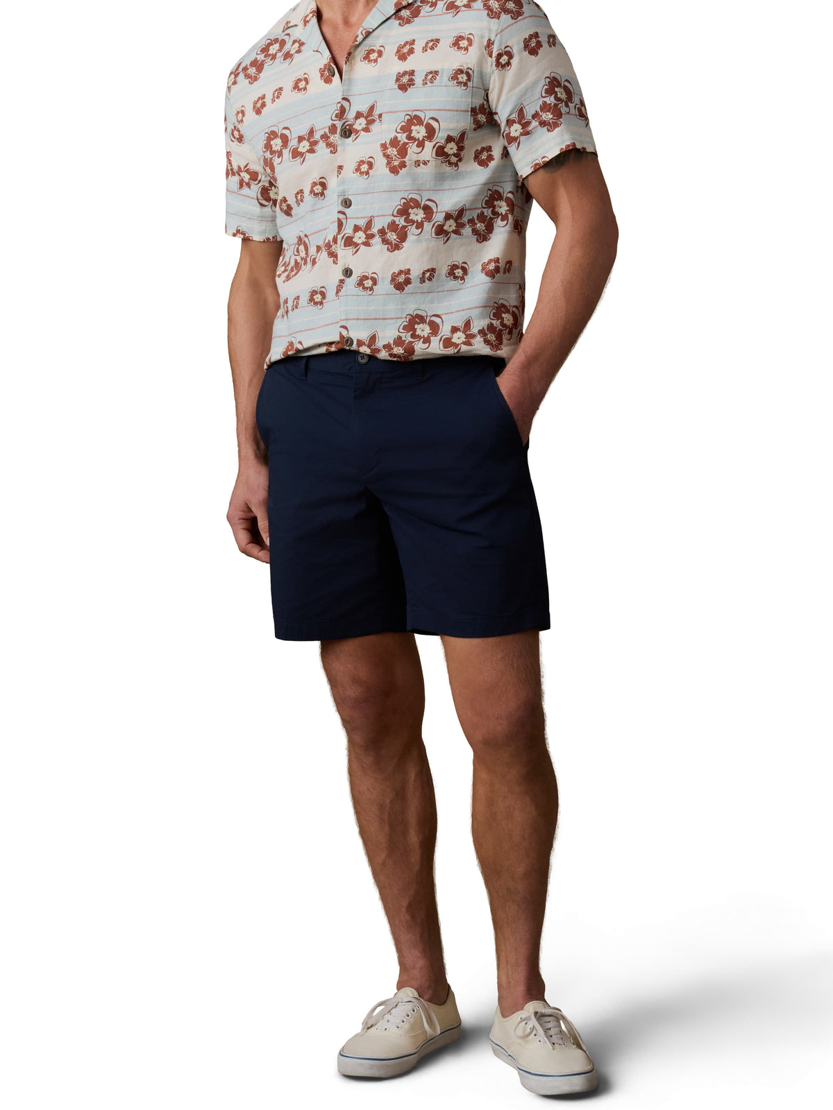 A man wearing a printed button up shirt, navy shorts, and white sneakers, image 2 of 3