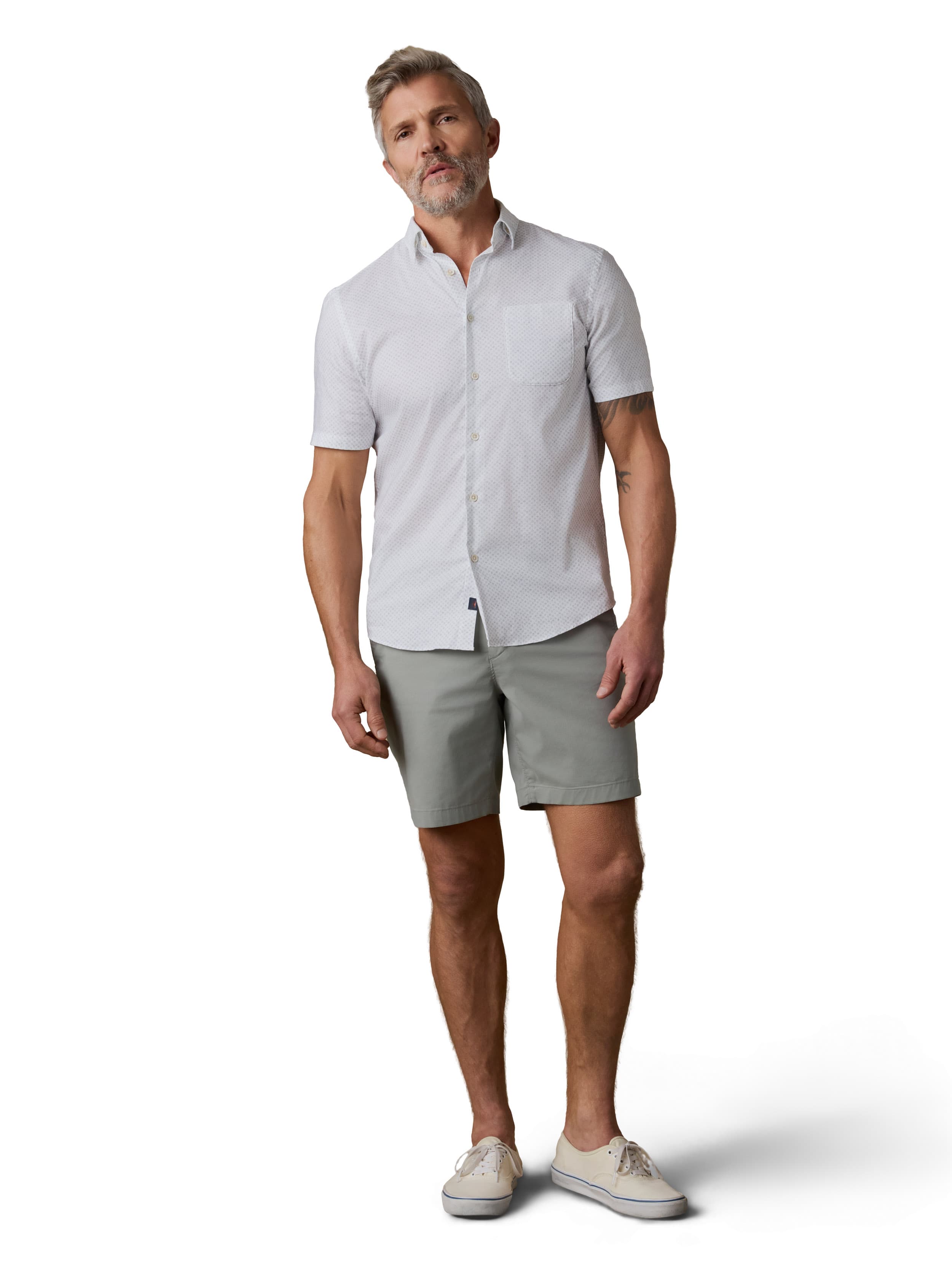 A man wearing a white button up shirt, sage green shorts, and sneakers