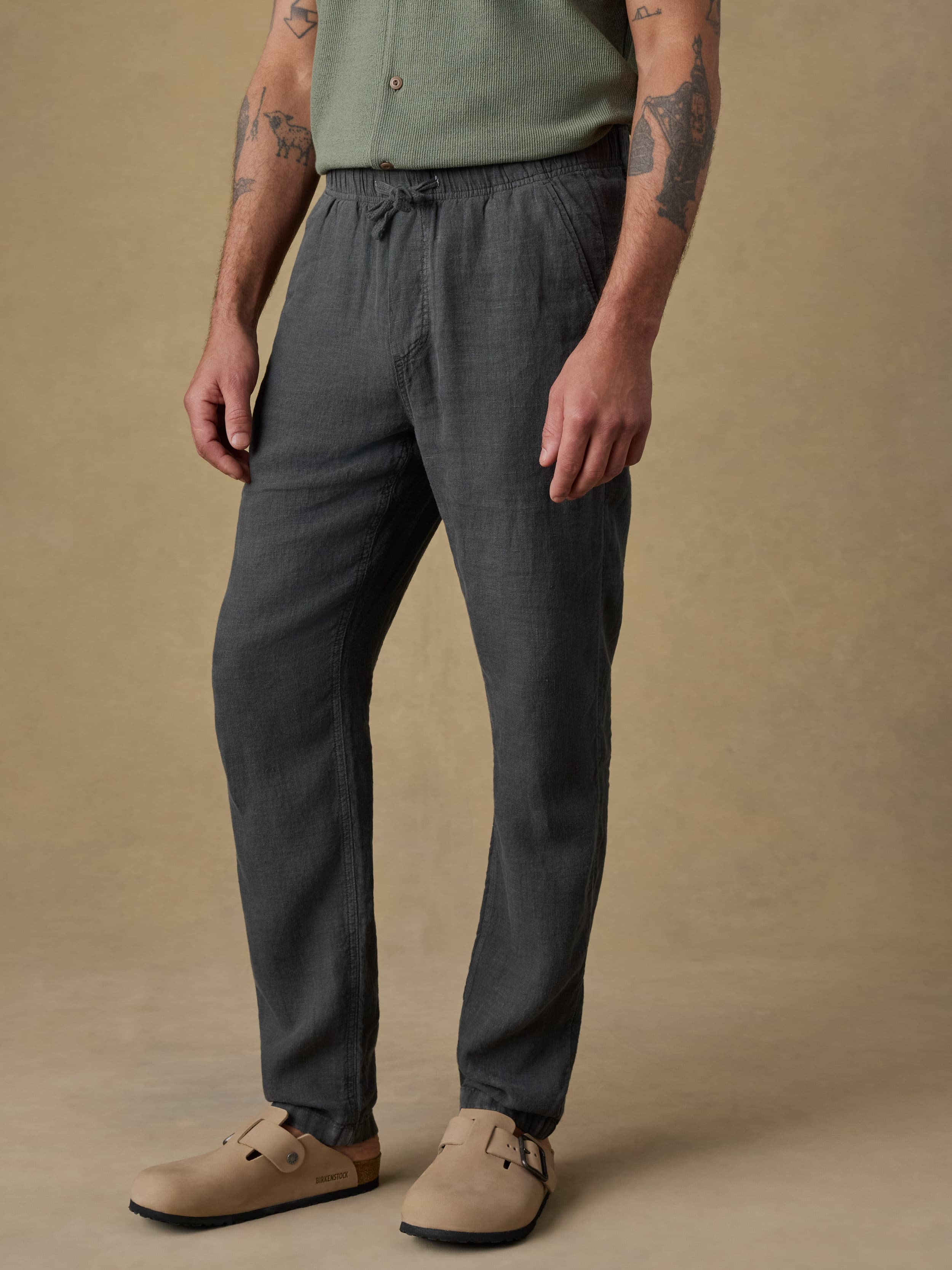 Man wearing black linen pants and a green shirt on a beige background