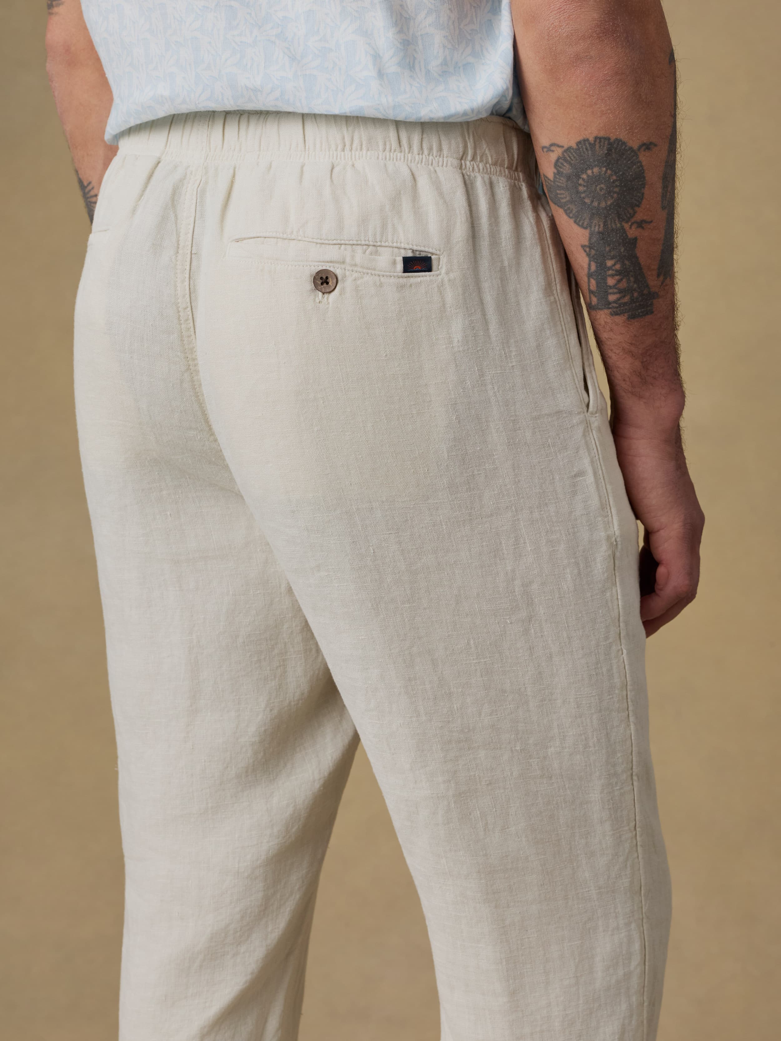 Man wearing a light blue linen shirt and beige linen pants against a beige background