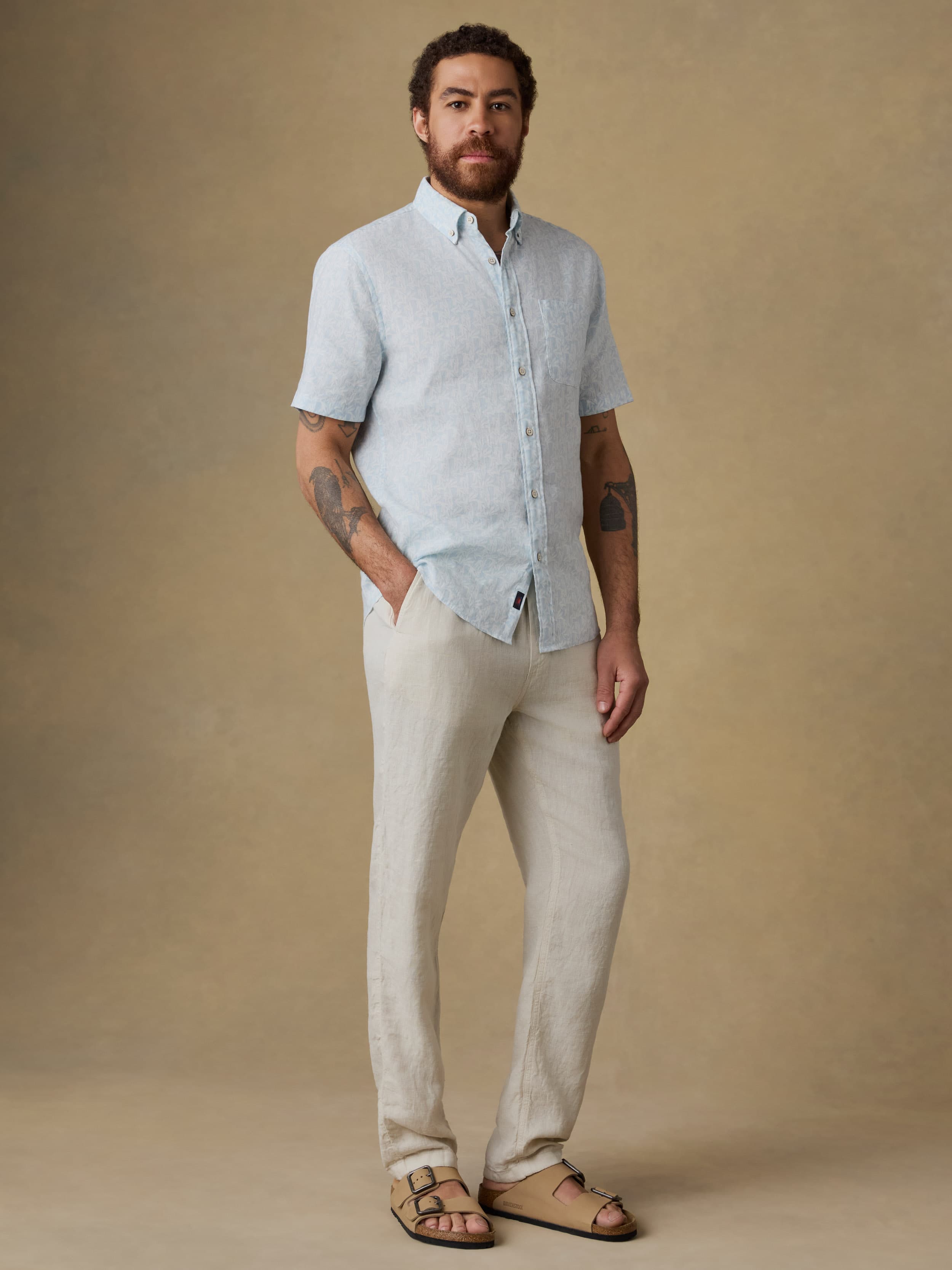 Man wearing a light blue linen shirt and beige linen pants against a beige background