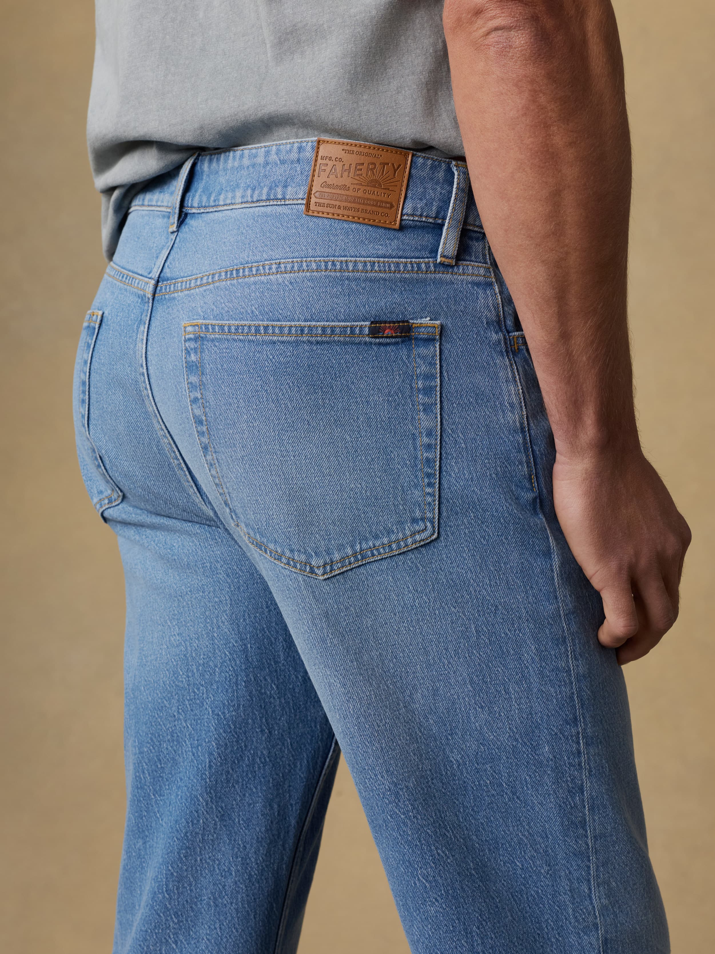 Detail back view of a man wearing a gray short sleeve t-shirt and blue jeans against a beige background