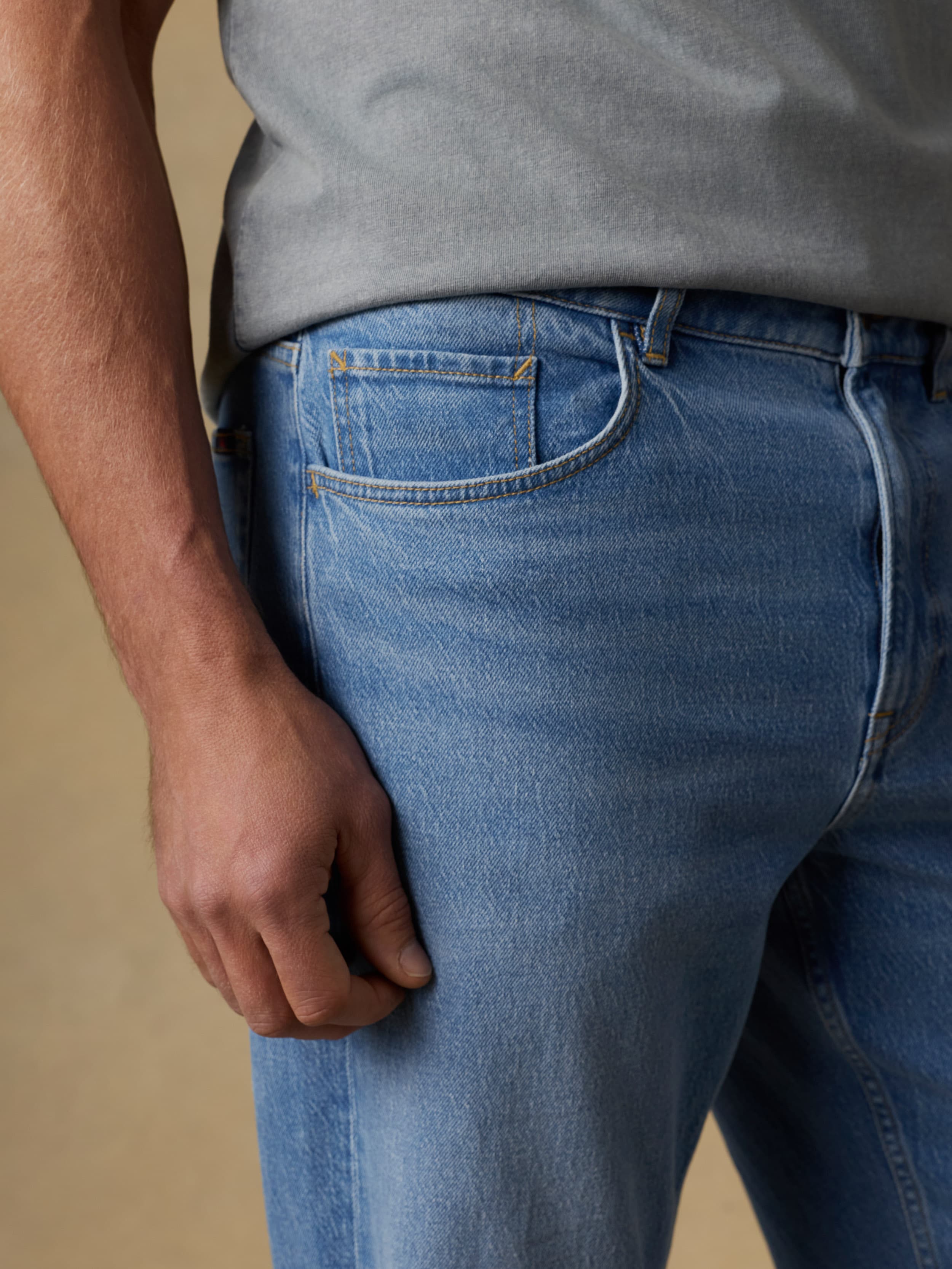Man wearing a gray short sleeve t-shirt and blue jeans against a beige background