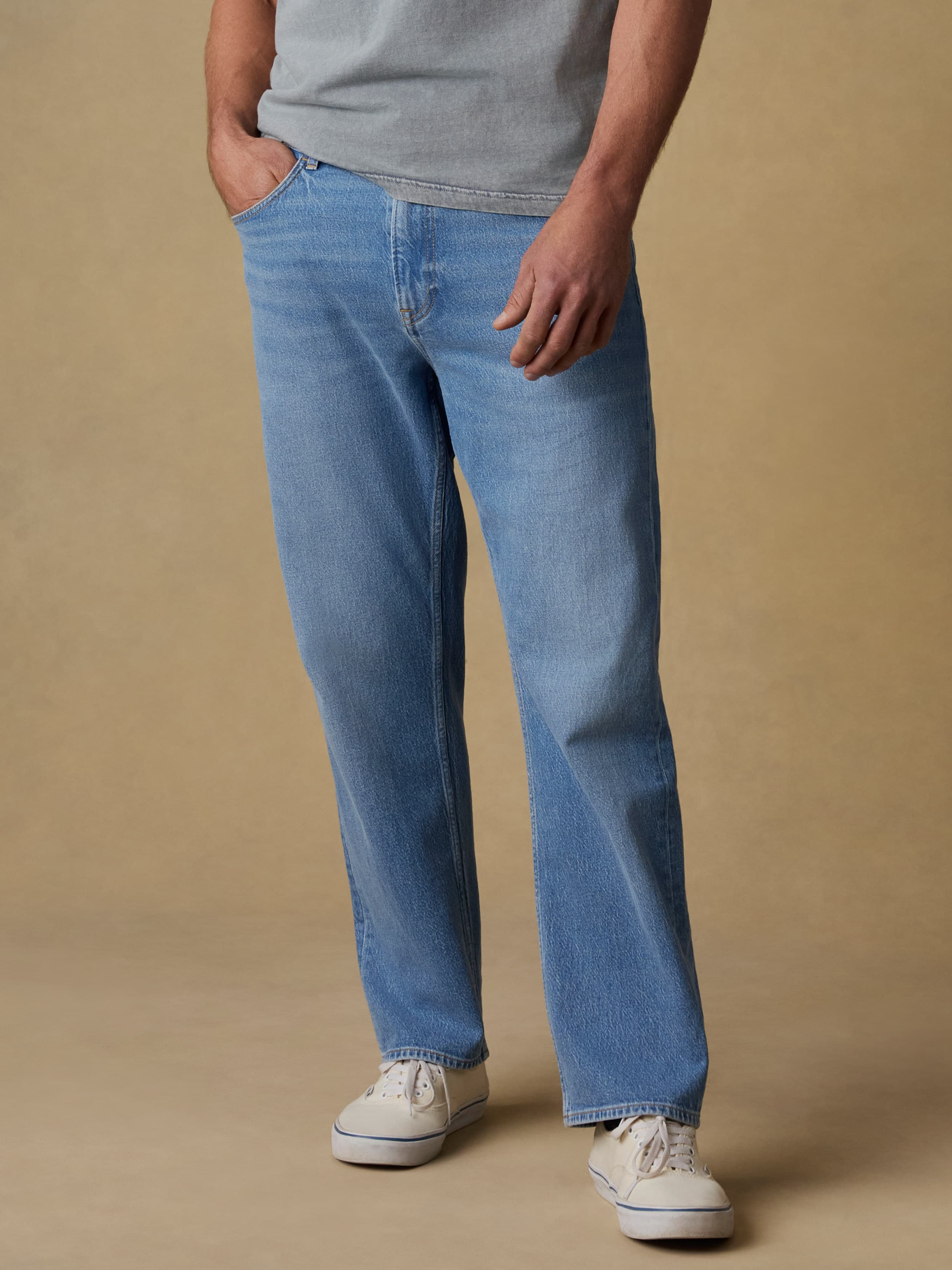 Man wearing a gray short sleeve t-shirt and blue jeans against a beige background