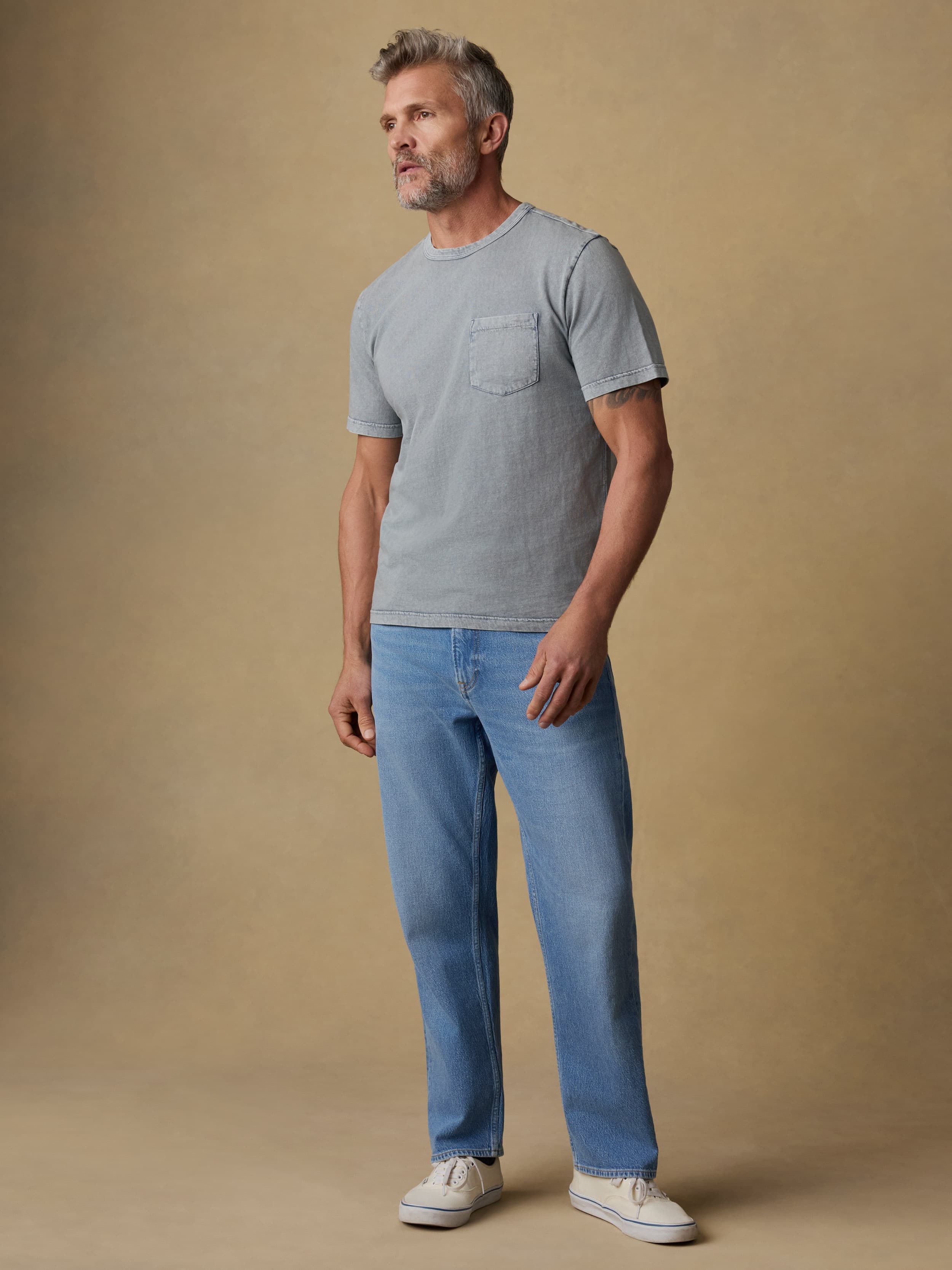 Man wearing a gray short sleeve t-shirt and blue jeans against a beige background