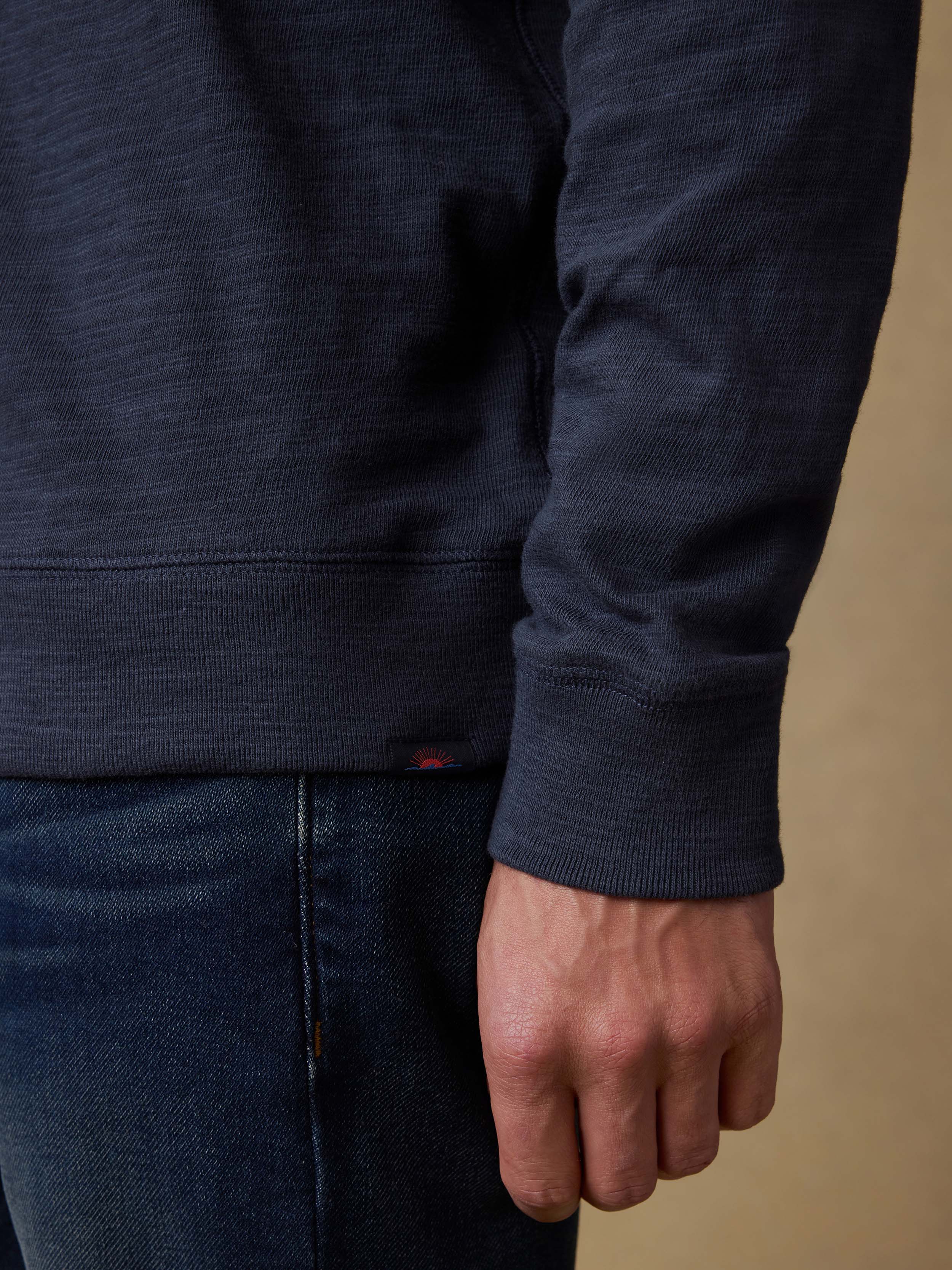 Man wearing a navy blue hoodie and jeans against a beige background