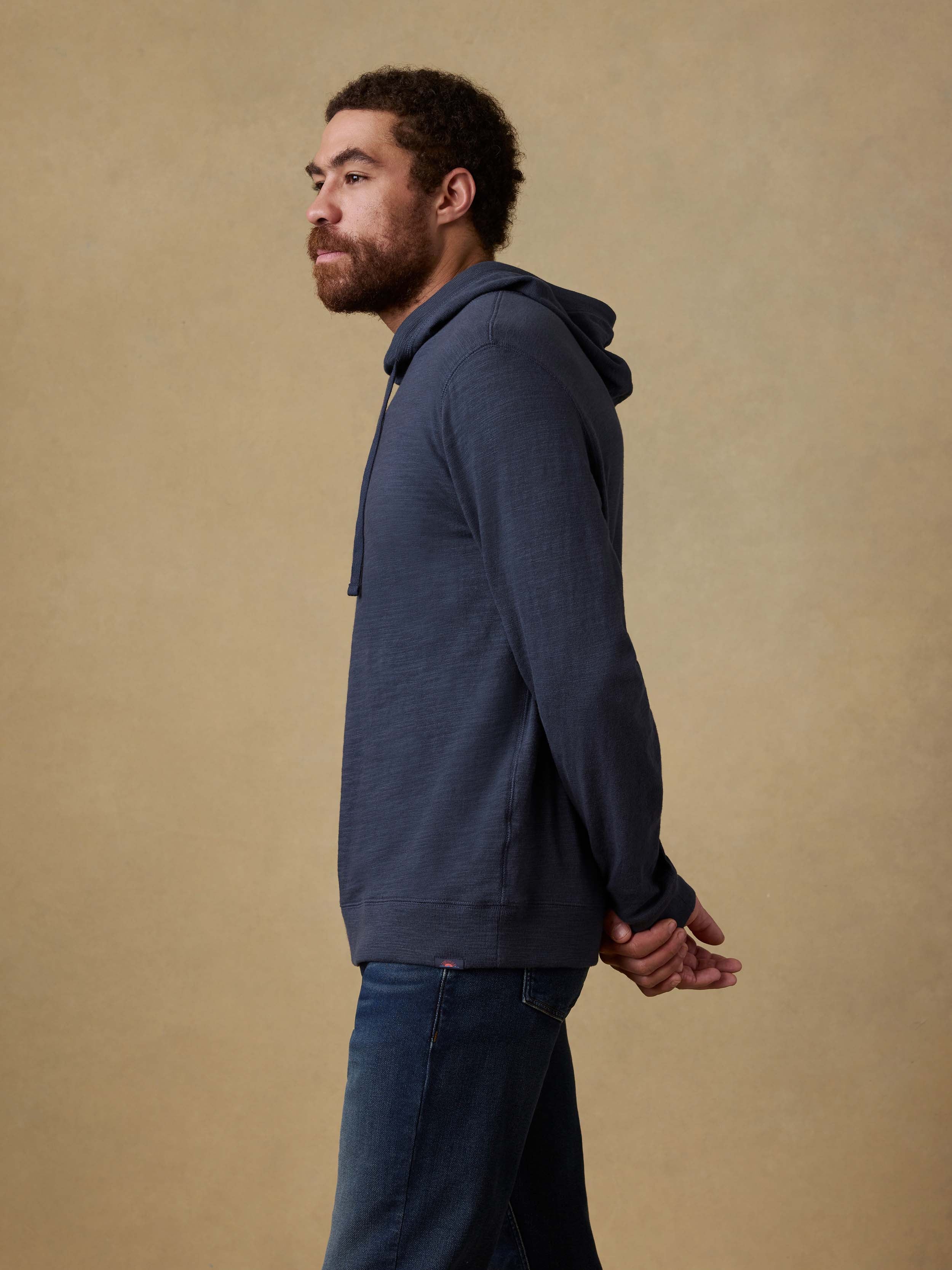 Man wearing a navy hoodie and blue jeans against a beige background