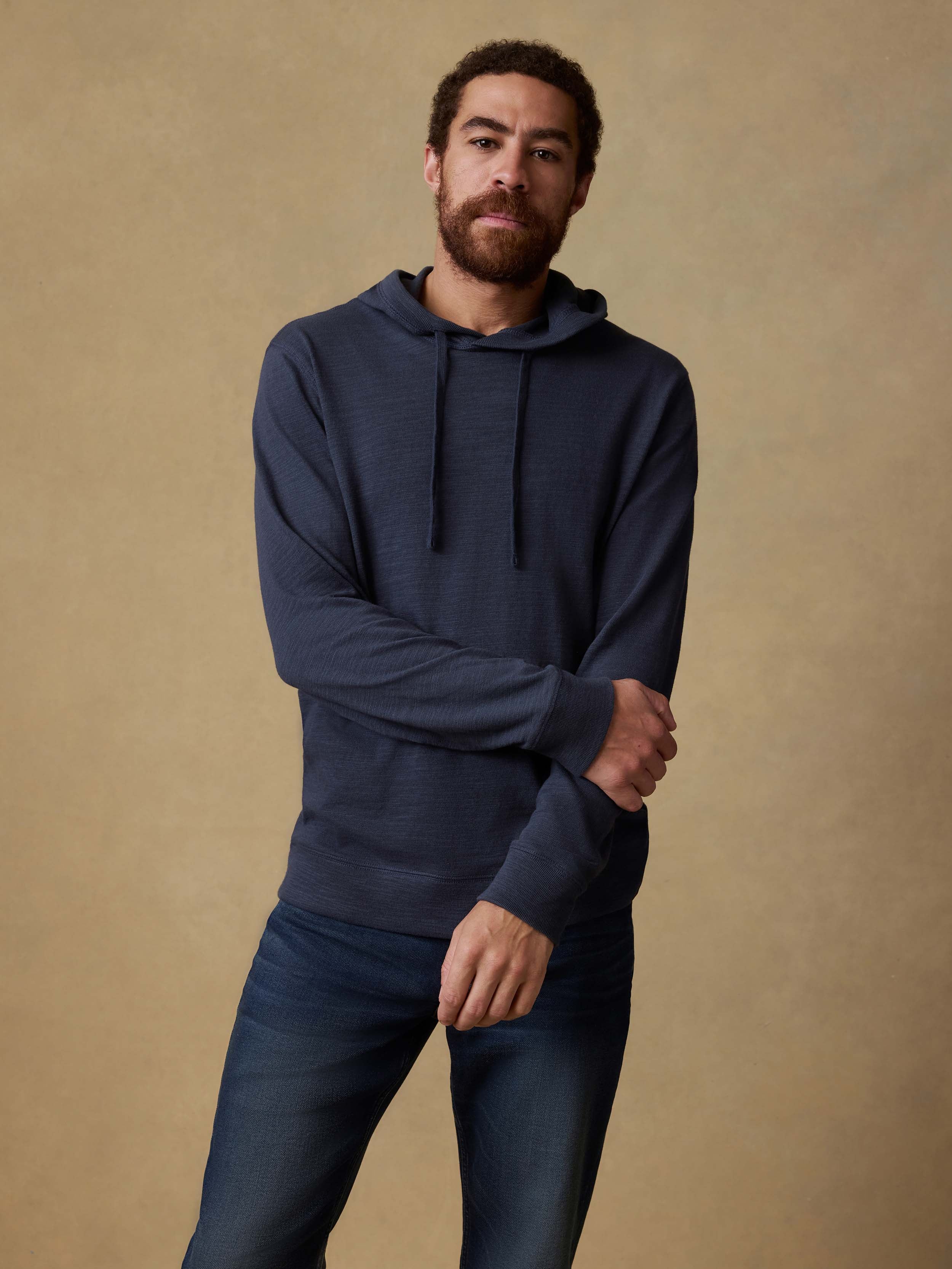 Man wearing a navy hoodie and blue jeans against a beige background