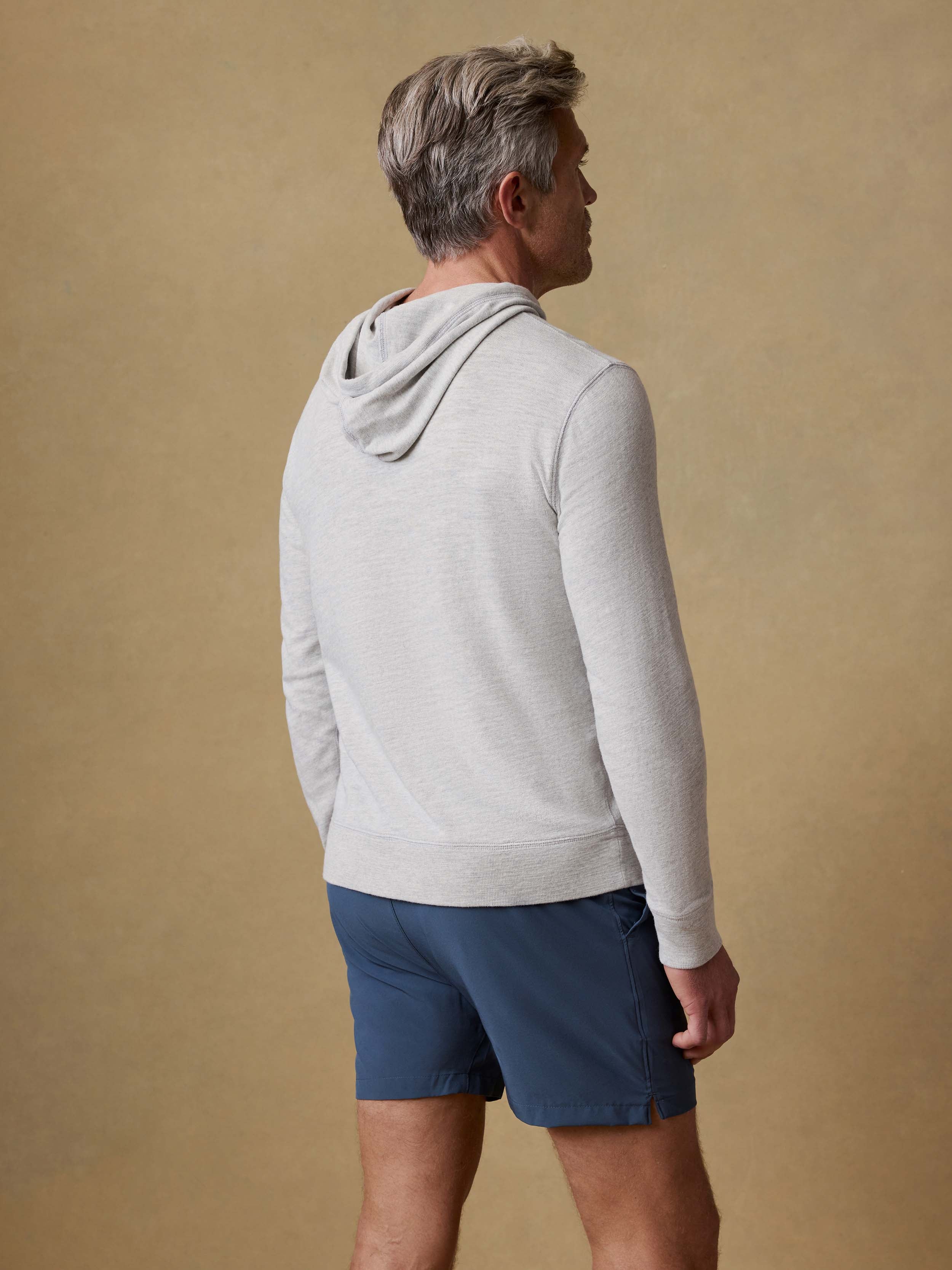 Back view of a man wearing a gray hoodie and blue shorts against a beige background