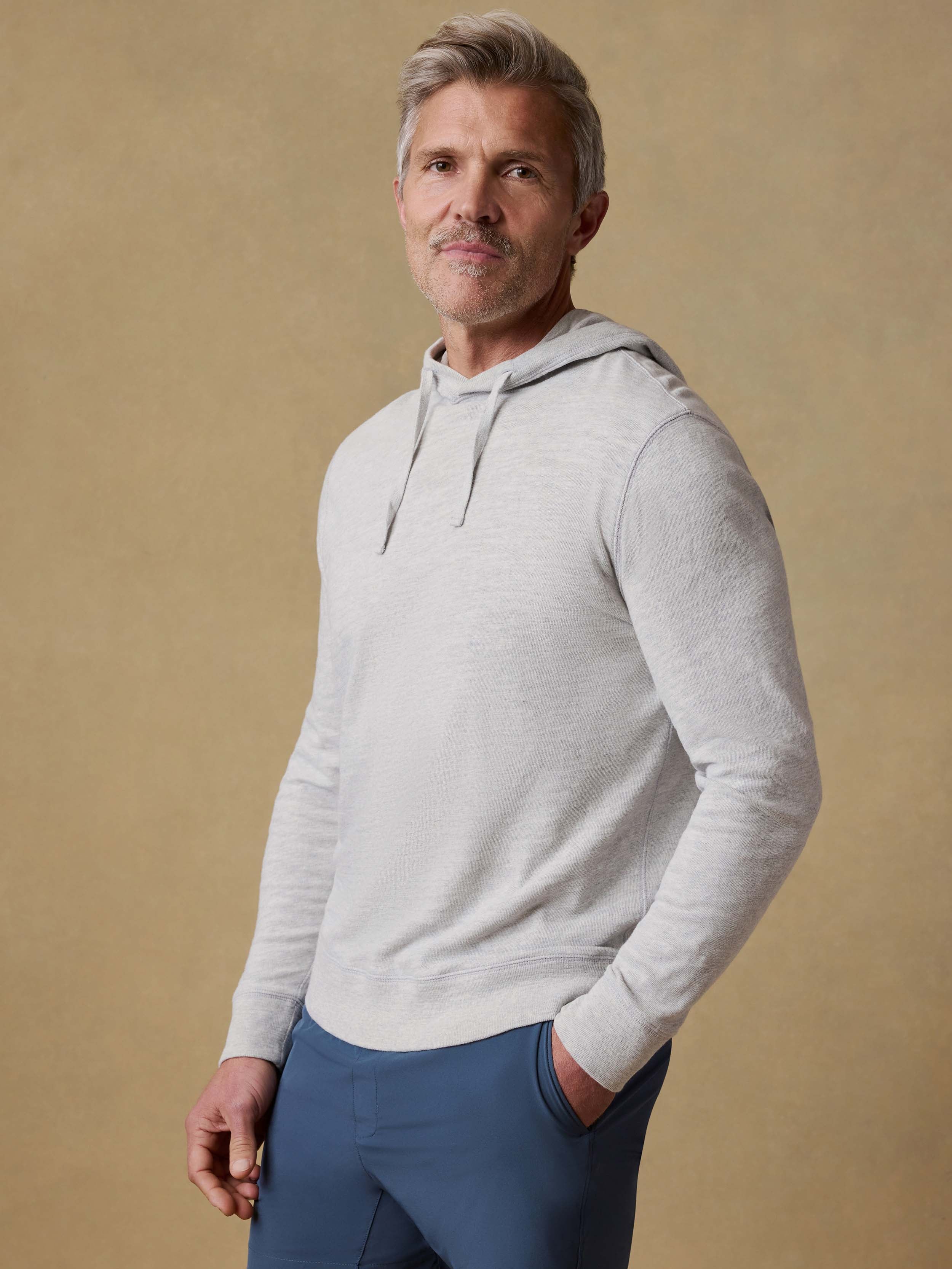 Man wearing a gray hoodie and blue shorts against a beige background