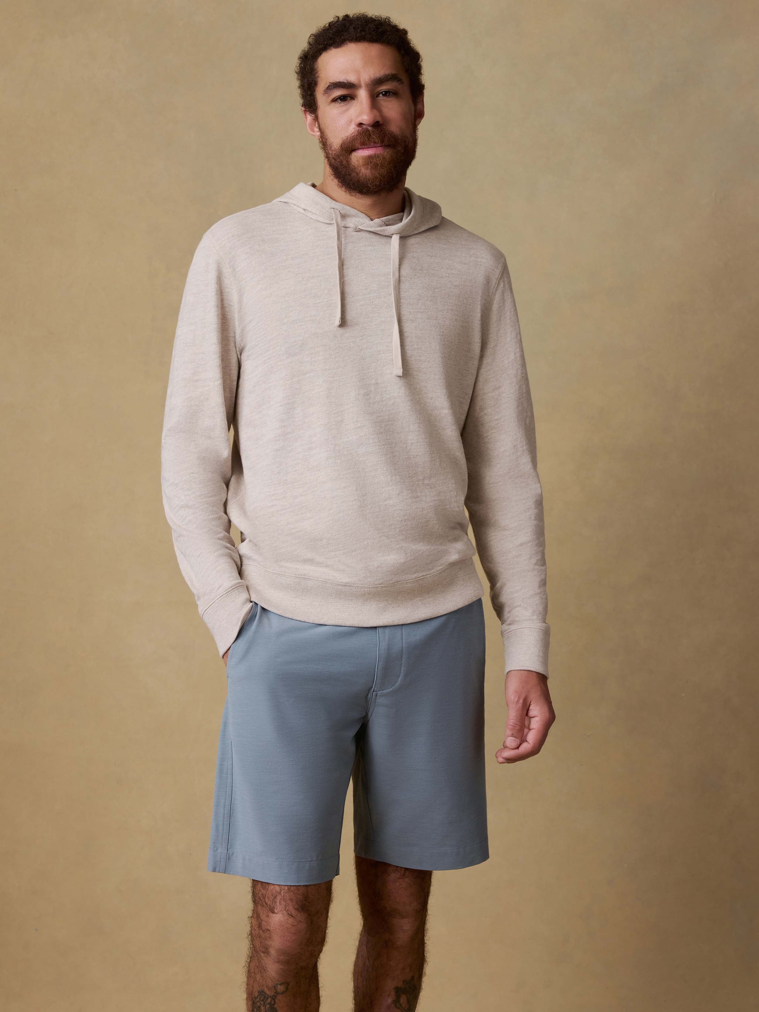 Man wearing a beige hoodie and light blue shorts against a beige background