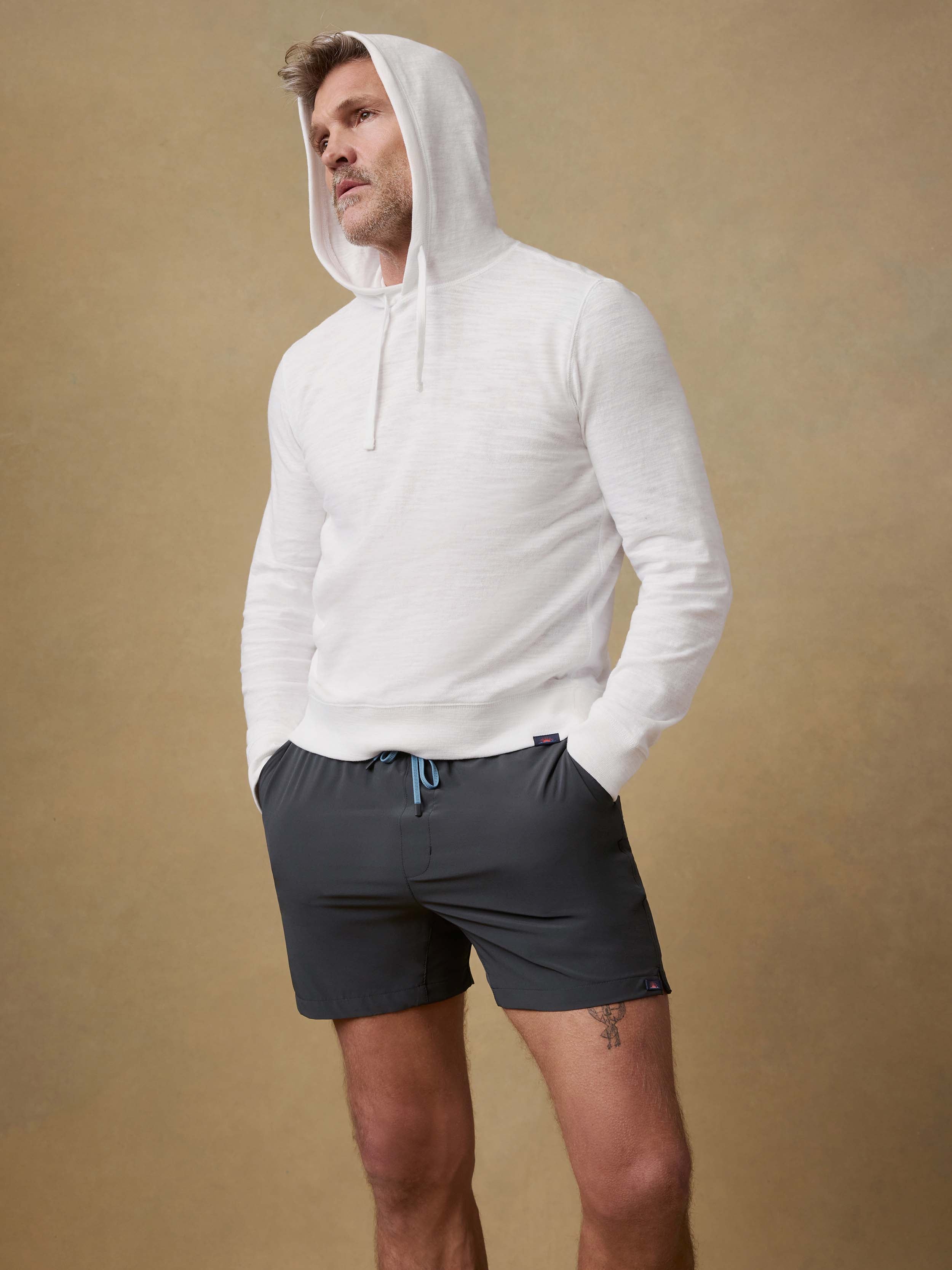Man wearing a white hoodie and black shorts against a beige background