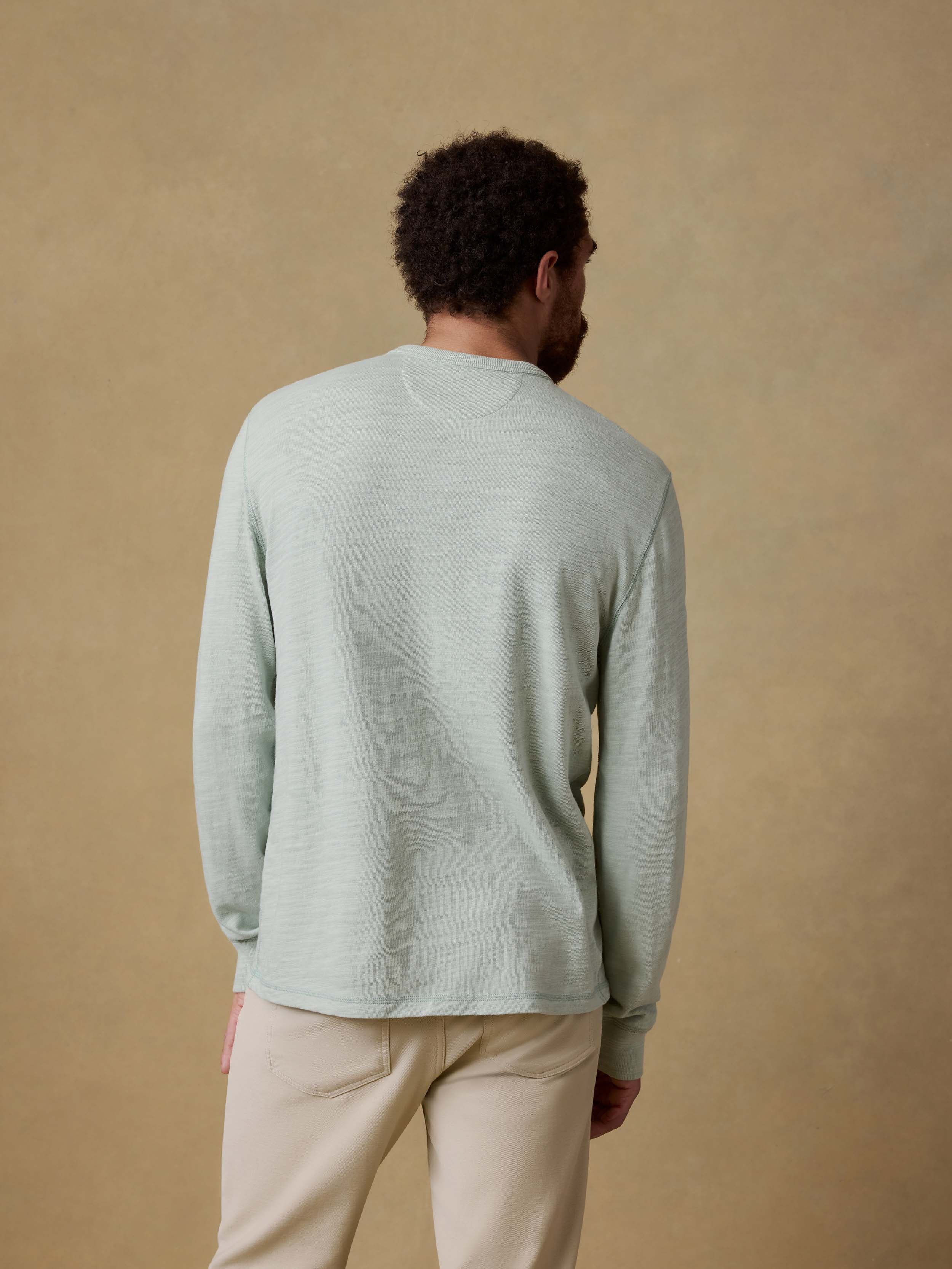 Back view of a man wearing a light green long-sleeve shirt against a beige background