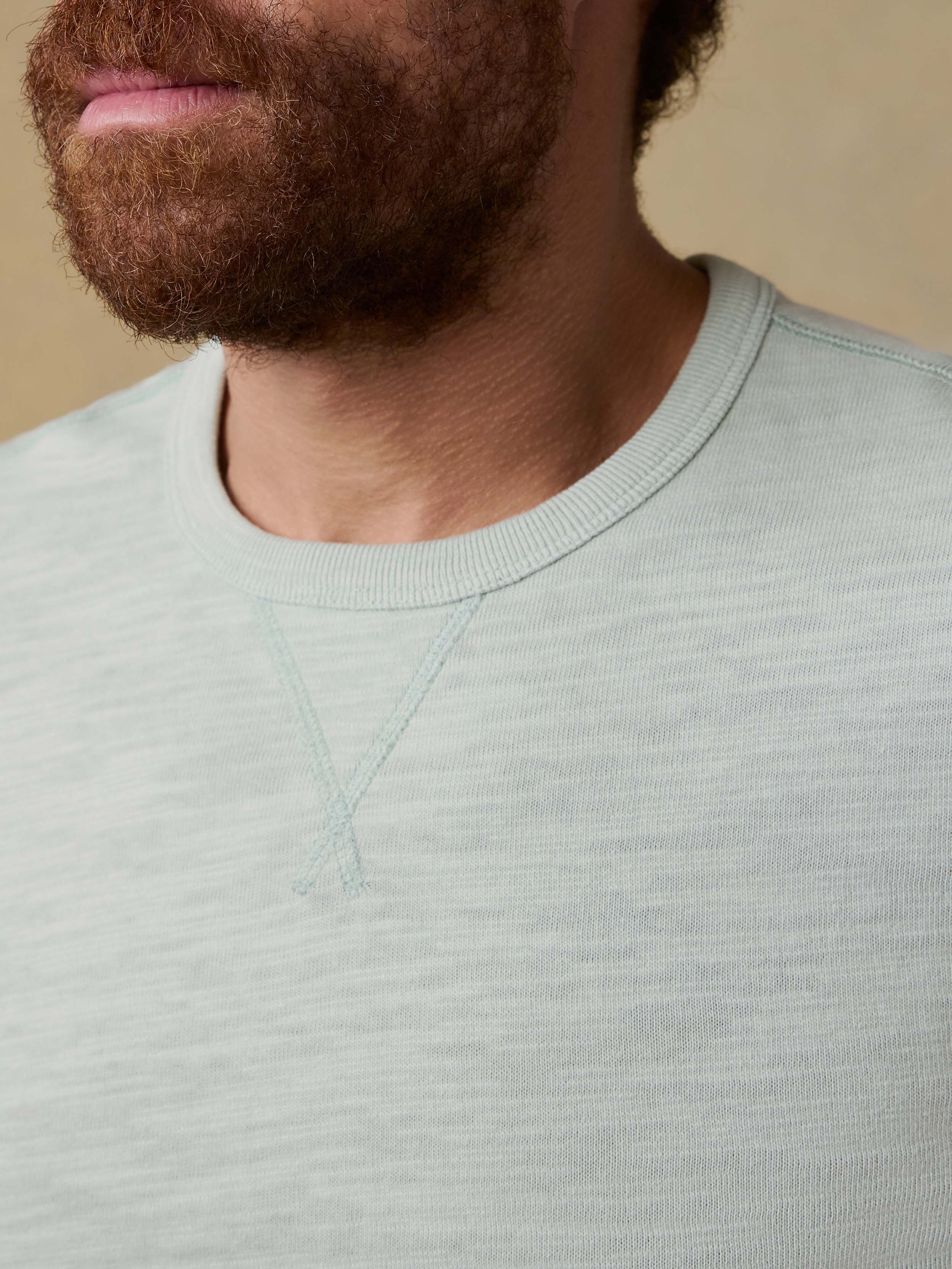 Detail view of a man wearing a light green long-sleeve shirt against a beige background