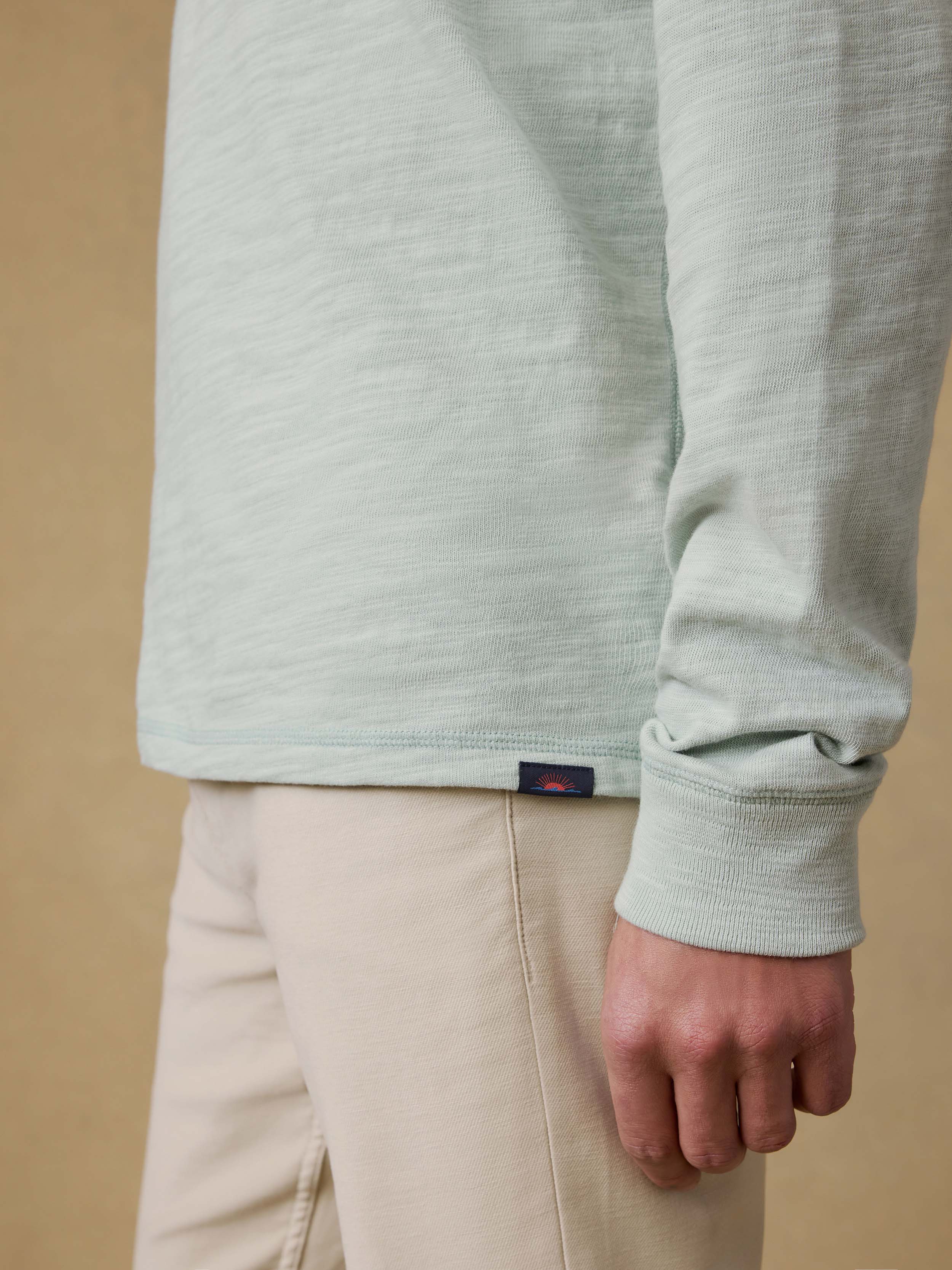 Detail view of a man wearing a light green long-sleeve shirt against a beige background