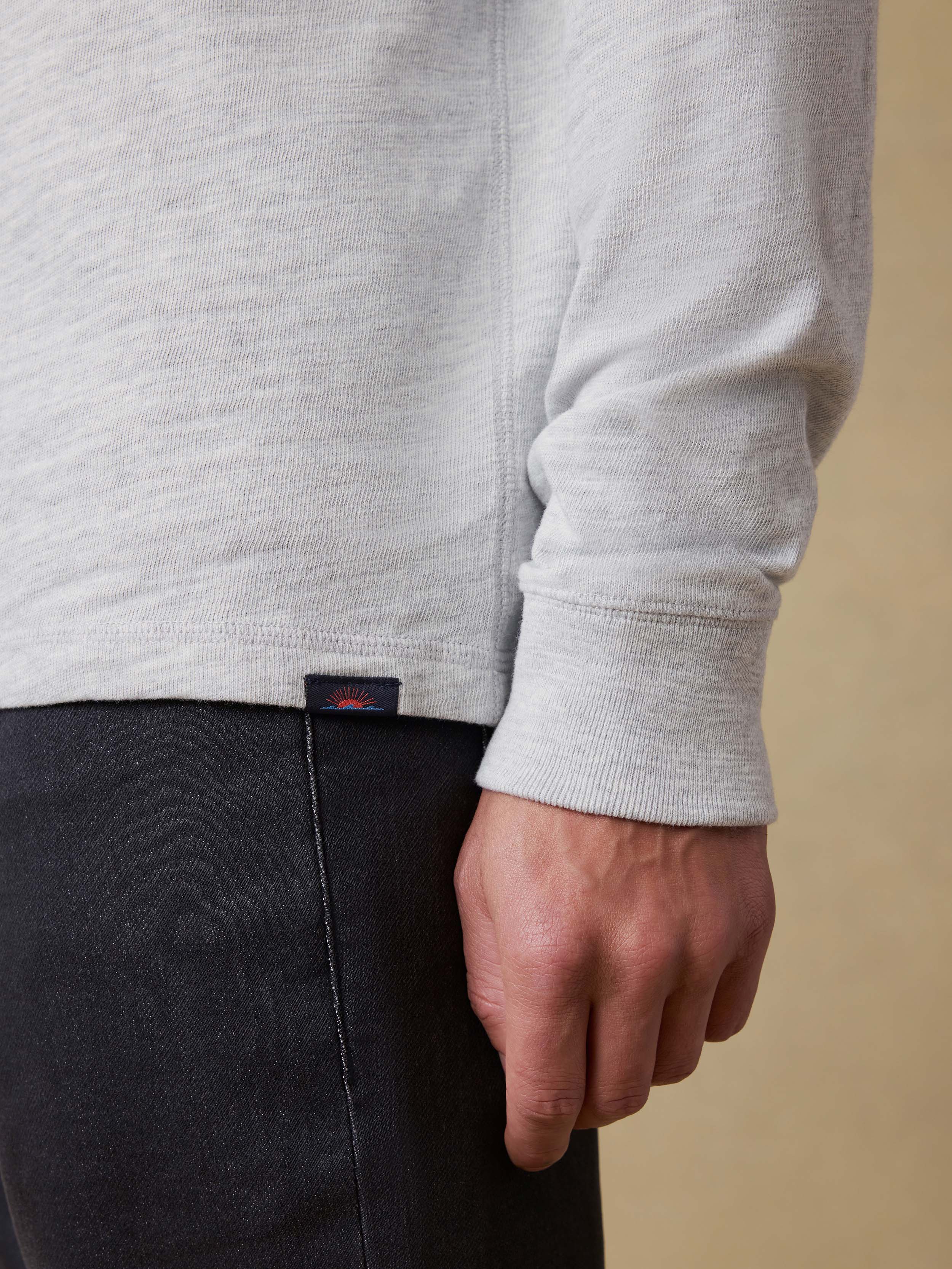 Detail shot of a man wearing a light gray long sleeve shirt and dark pants against a beige background